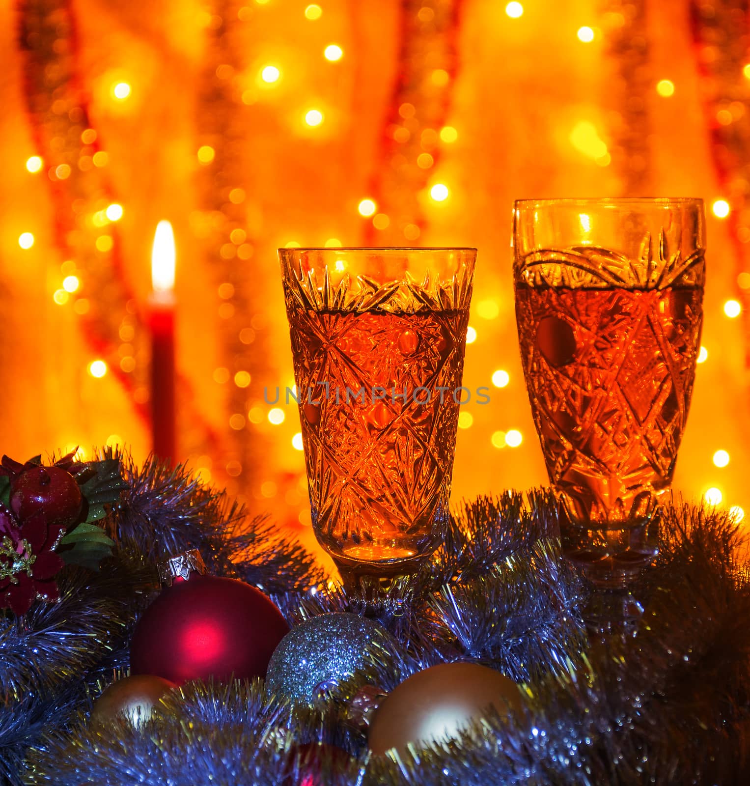 Some wine glasses of champagne lying Christmas balls and tinsel. On blurred background is visible burning candle.

