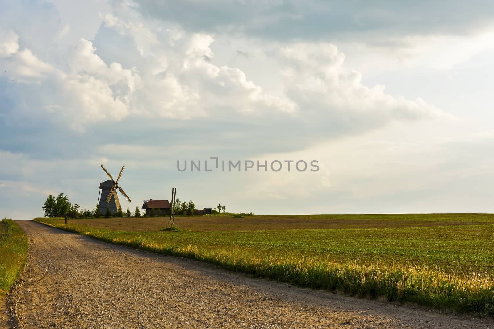 Dirt road to the lonely windmill and farmhouse located among the by Grommik