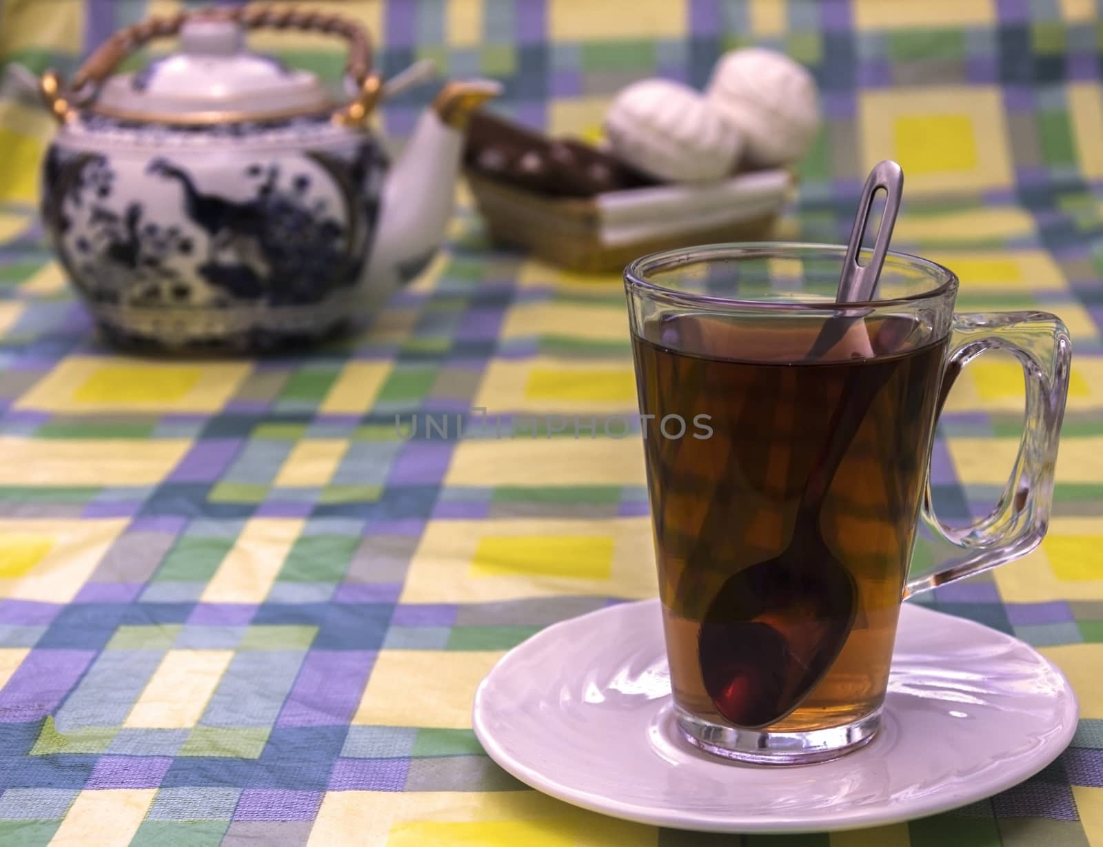 In the foreground is a glass cup with tea. In the background can be seen tea and sweets