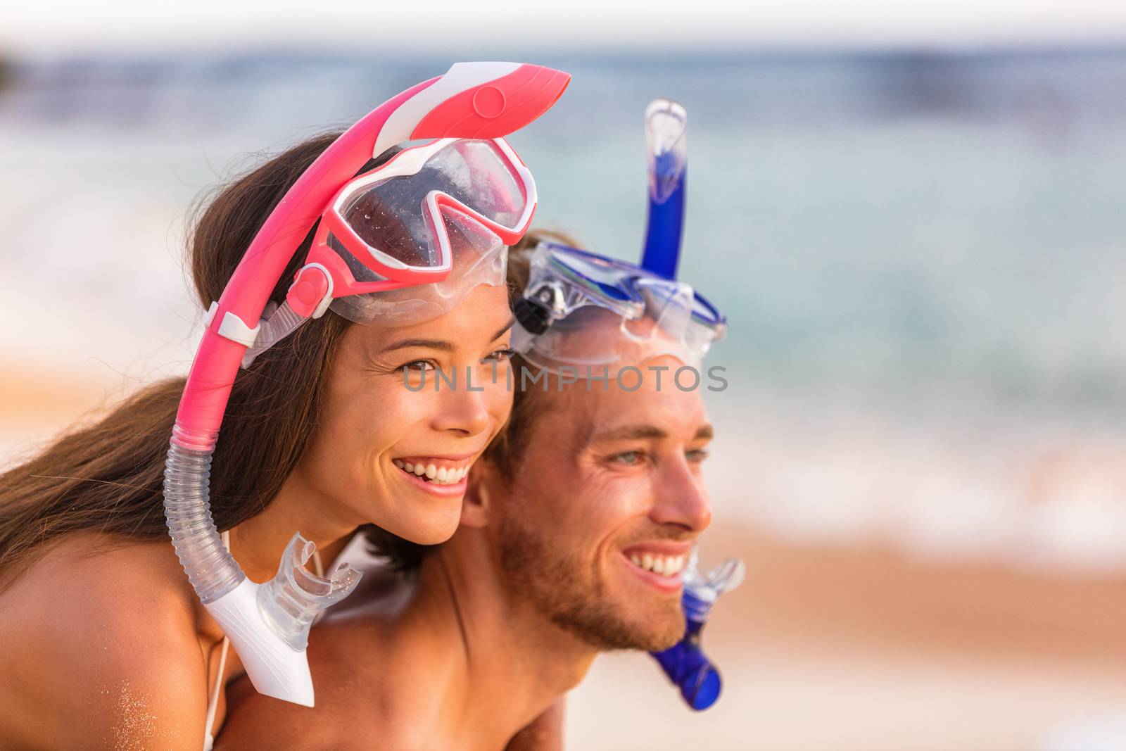 Beach travel people having fun snorkeling. Happy young interracial couple on beach with snorkel mask looking at copy space after swimming on summer vacation. Asian woman, Caucasian man by Maridav