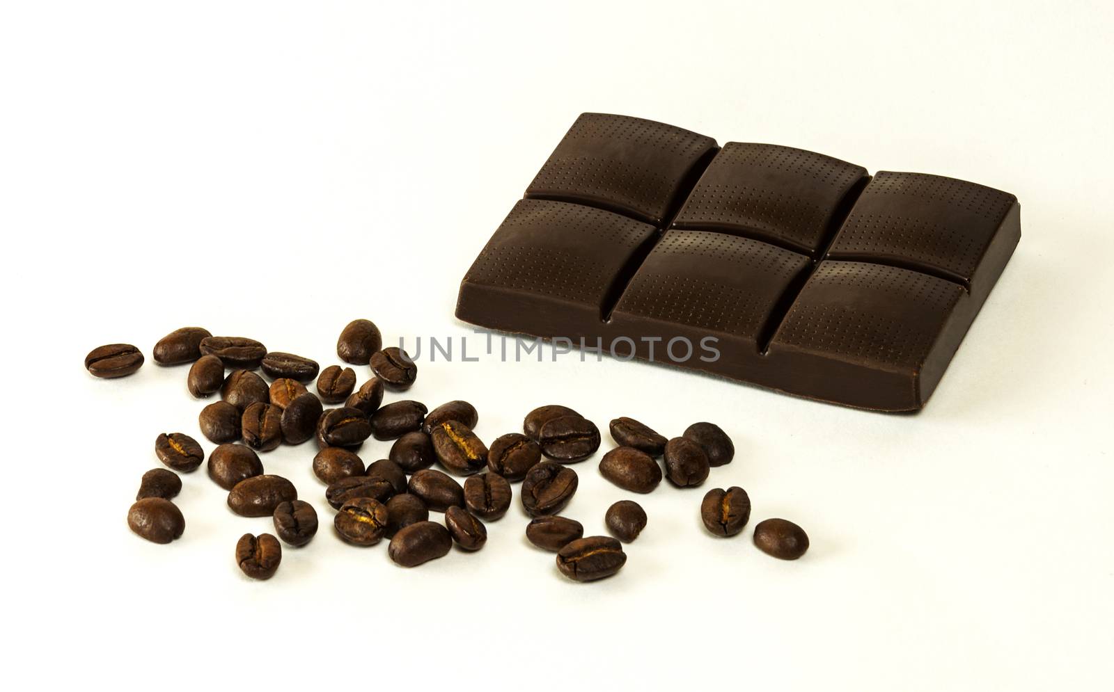 On a light background is dark chocolate tiles and scattered grains of coffee
