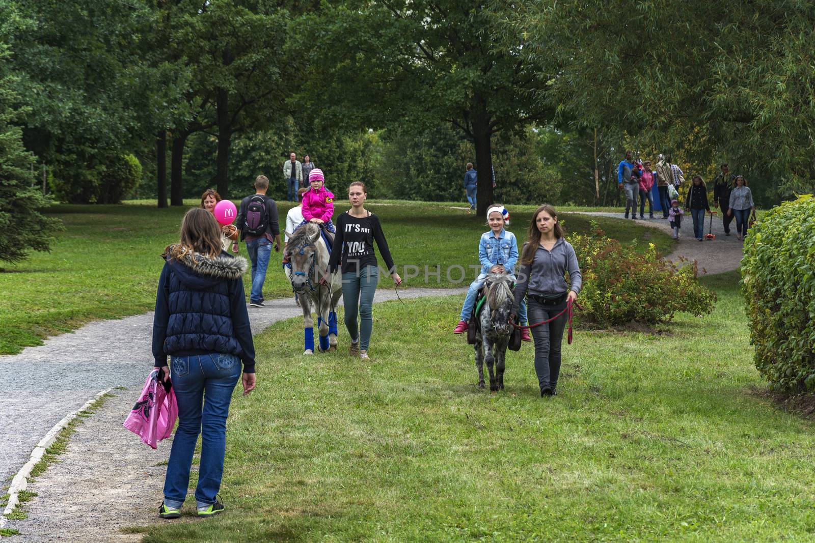 Children ride on horseback in the city park by Grommik