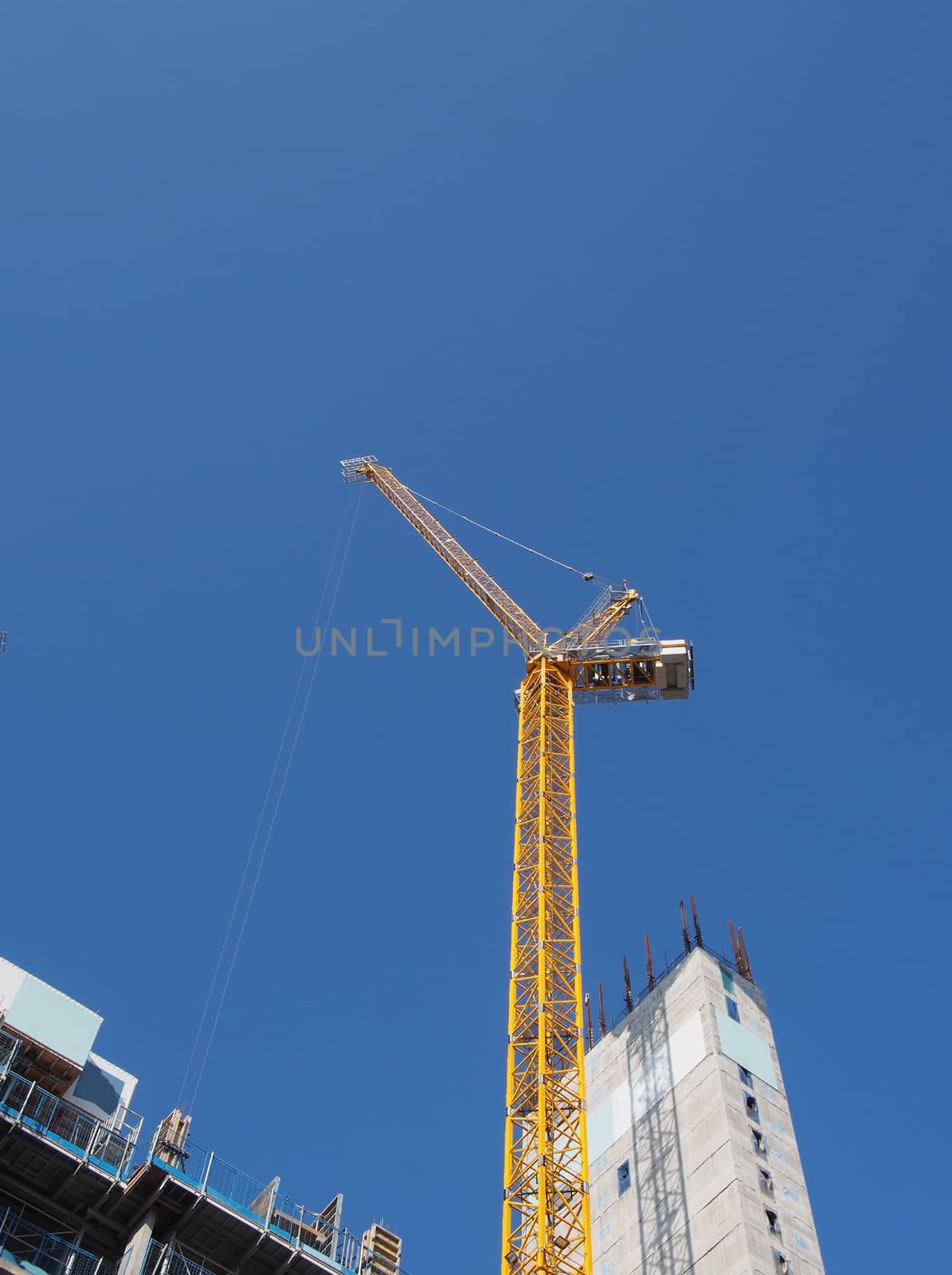 a view of a tall tower crane working on large construction sites against a blue sky