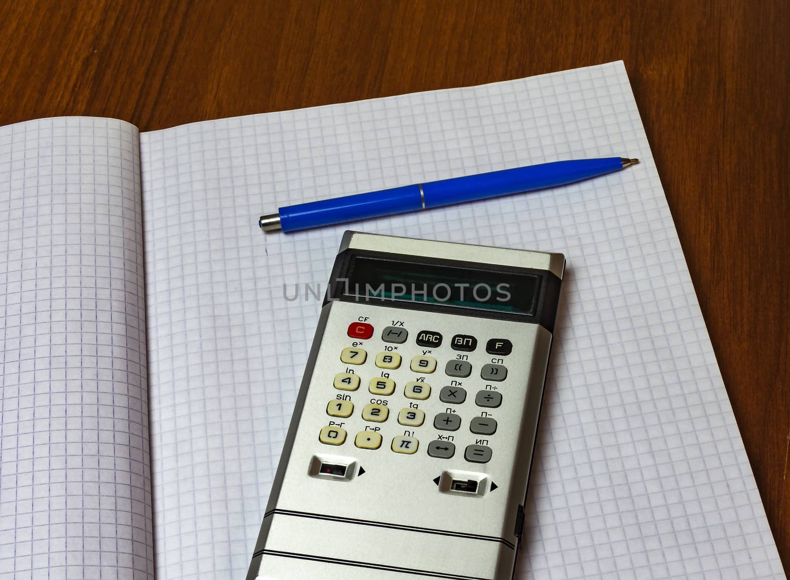 Blue pen and calculator lying on a sheet of paper into the cell from a notebook for records