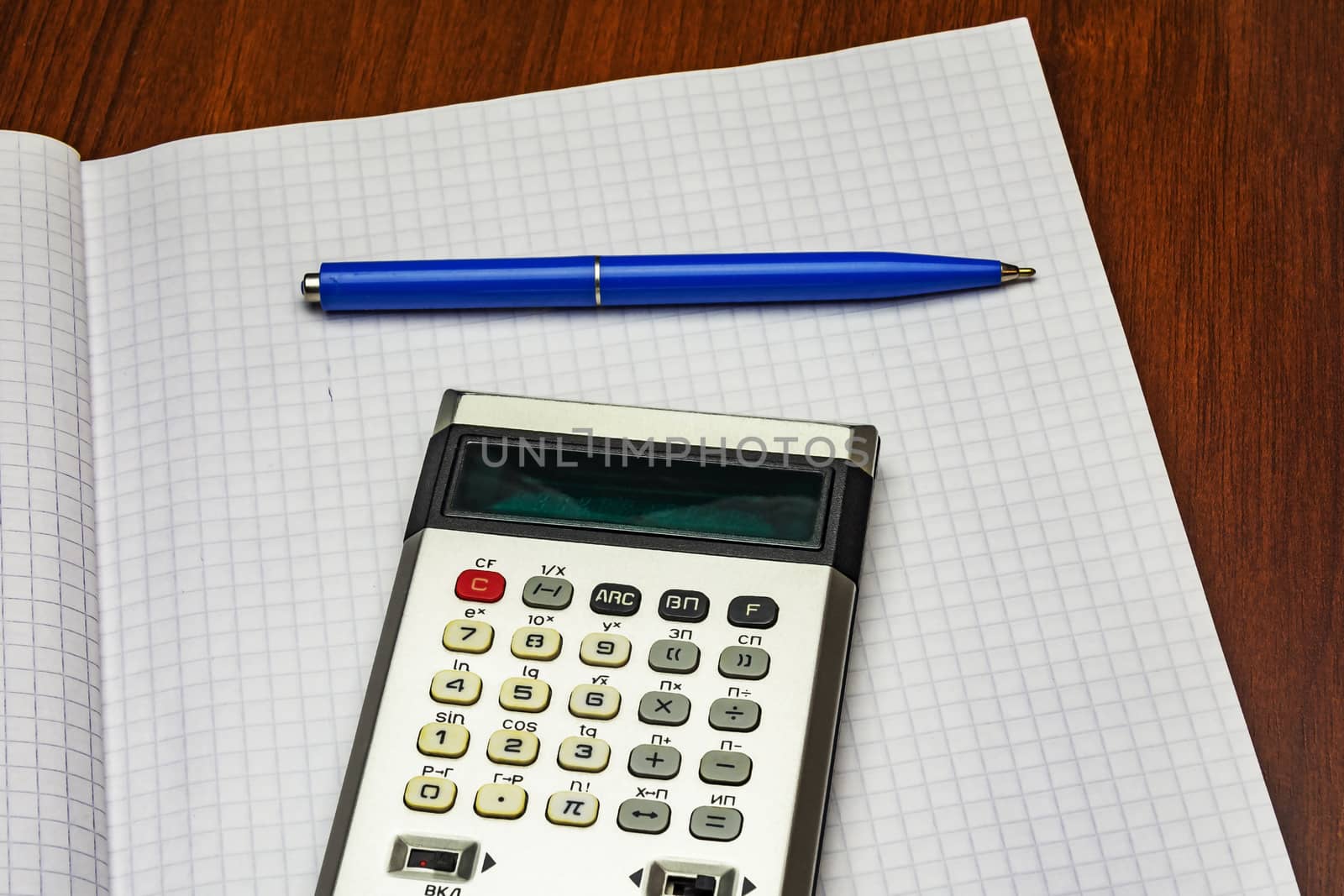 Calculator and blue ballpoint pen lie on a sheet of paper into the cell from a notebook for records