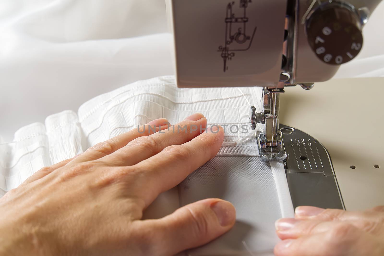 A woman works on a sewing machine. seamstress sews white curtains, close up view. by PhotoTime