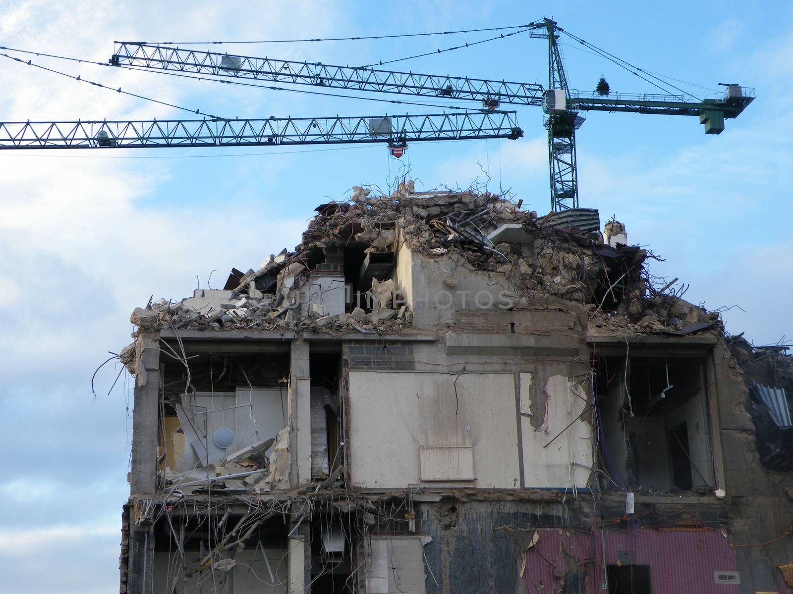 large cranes over a large concrete building being demolished with exposed walls during redevelopment of a large urban site