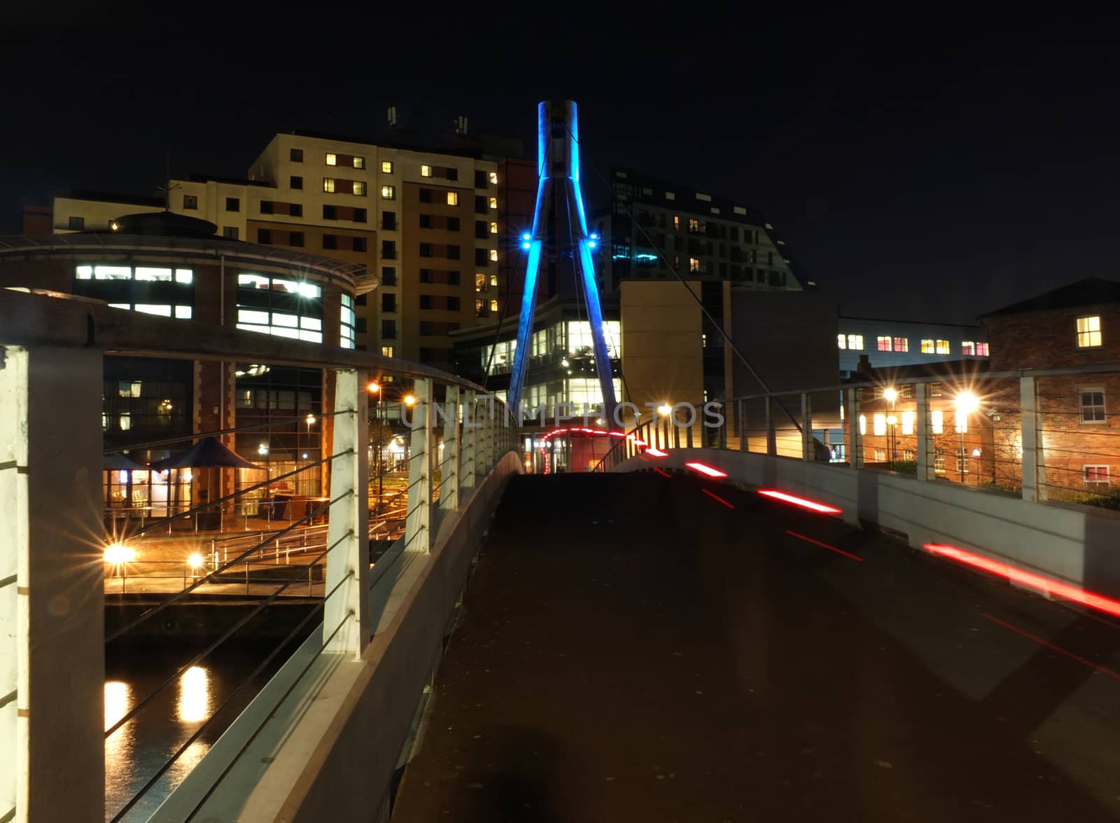 cityscape with the pedestrian footbridge crossing the river aire in leeds at night with bright lights and illuminated waterside buildings and light trails