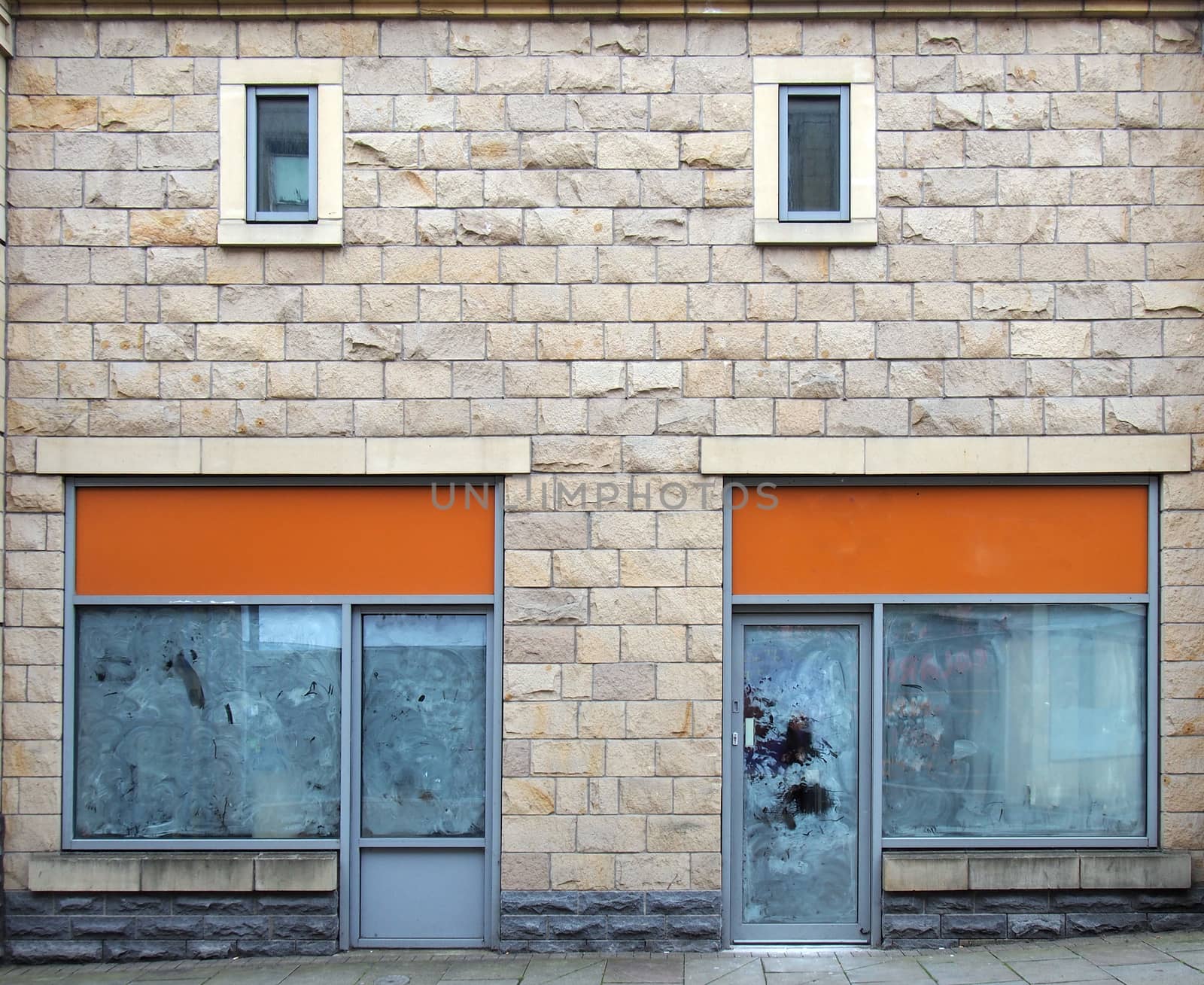 two empty abandoned shops on a street with whitewashed empty windows and blank store signs