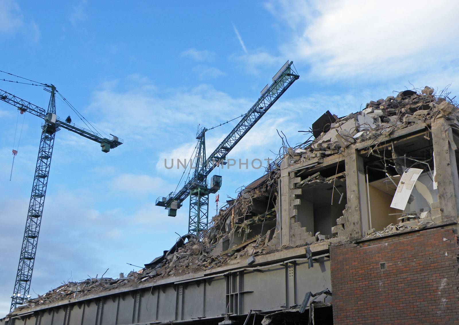 large cranes over a large concrete building being demolished with exposed walls during redevelopment of a large urban site