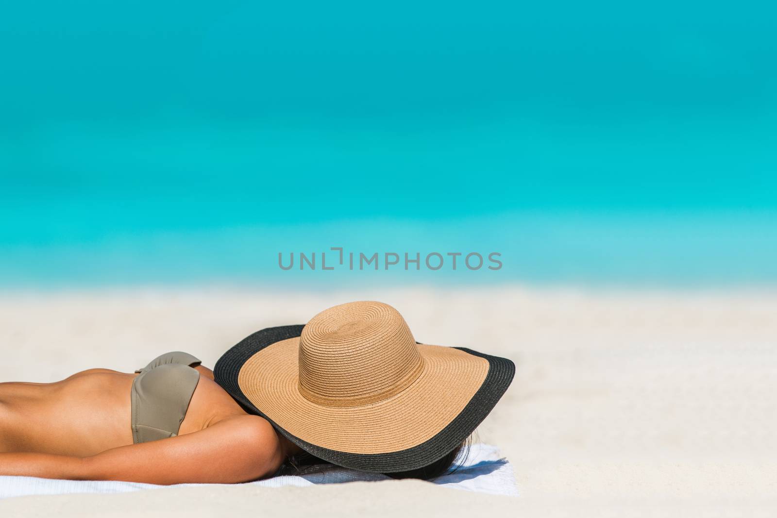 Beach woman sunbathing lying down sleeping covering her face with straw hat for uv sun rays protection on turquoise ocean background copyspace. Vacation girl relaxing tanning on summer travel.