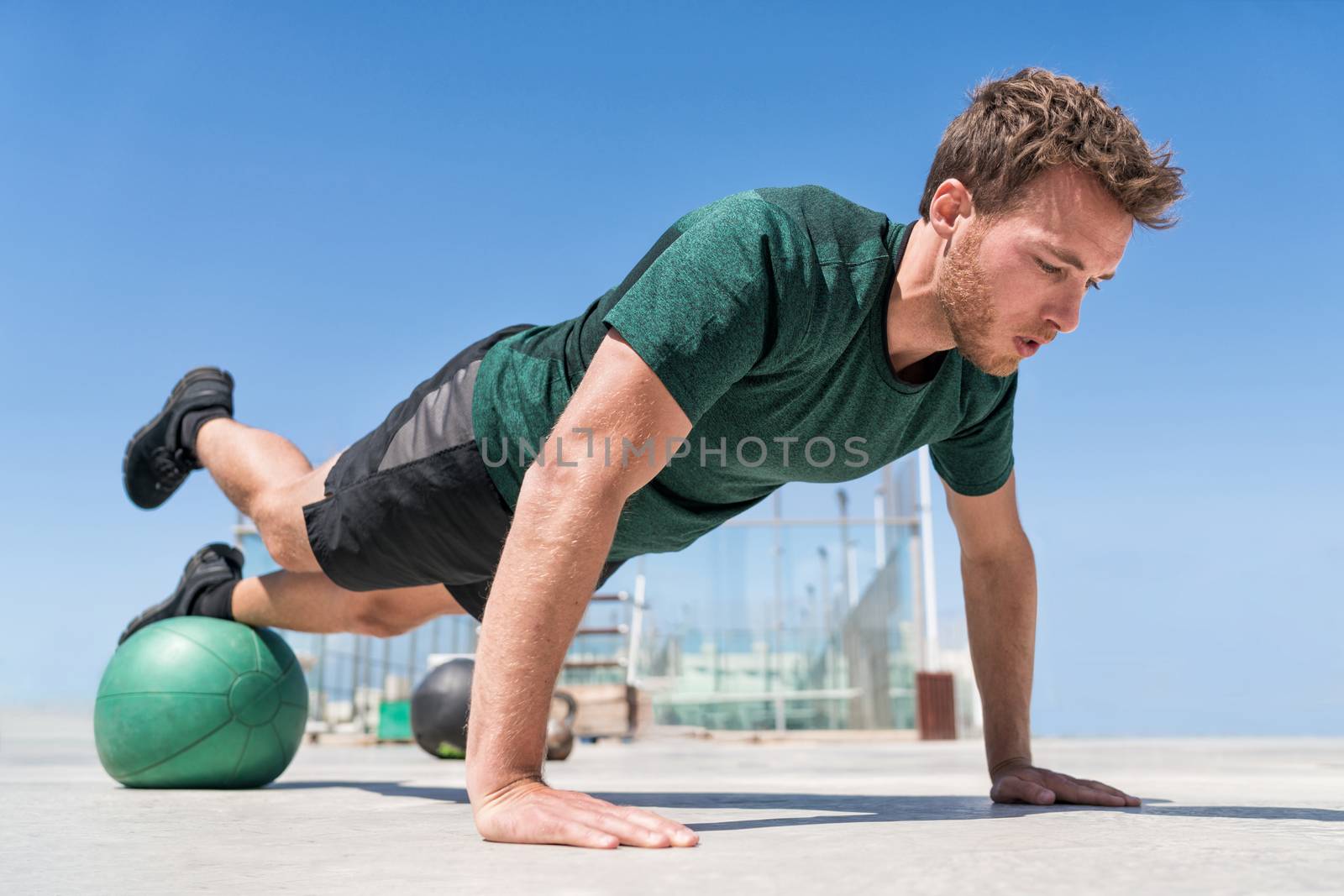 Man working out strength training doing incline push-ups workout at outdoor gym balancing on stability medicine ball with one leg raised. Bodyweight pushups exercises. Push-up variation.
