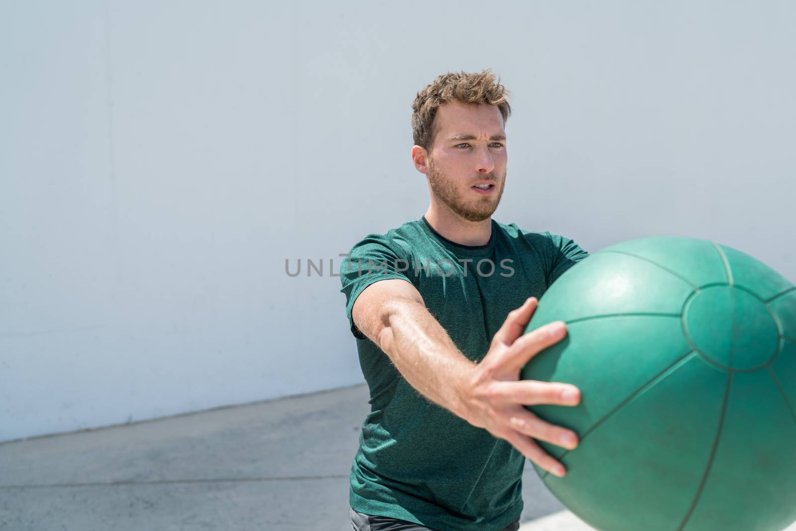 Medicine ball workout fitness man strength training arms doing deltoid front raise exercise for shoulder muscles at gym. Upper body workout with weight ball at fitness centre.