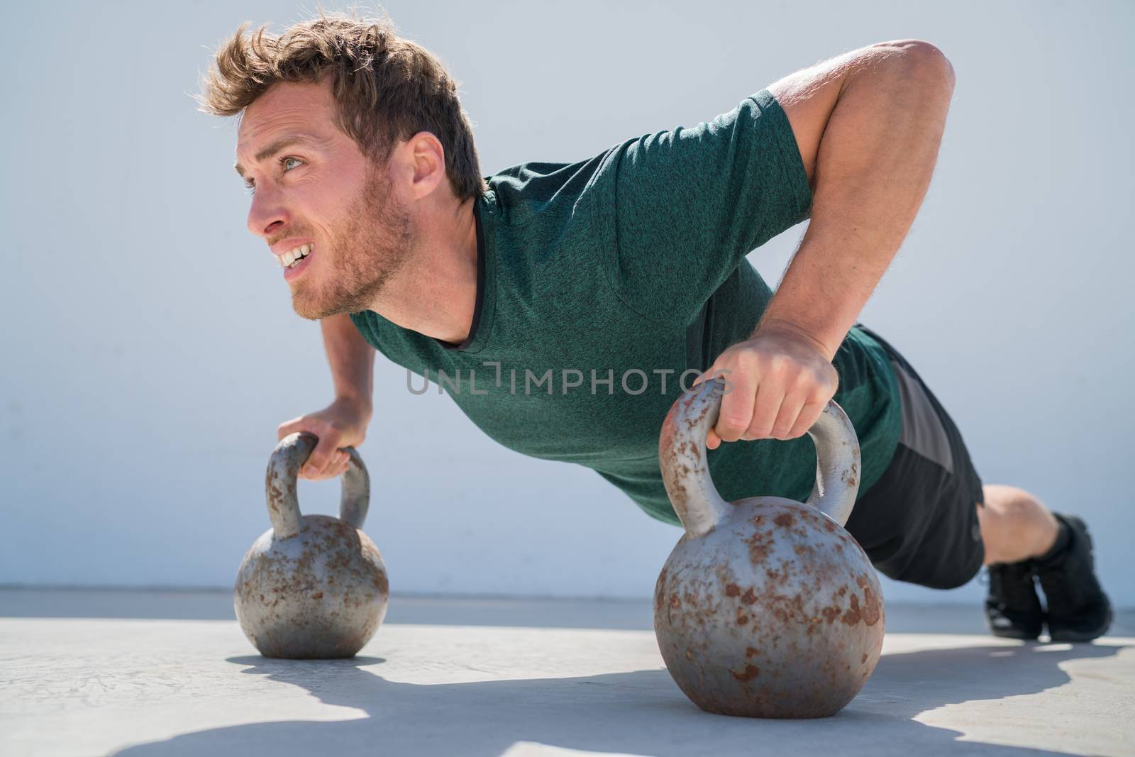 Fitness gym man doing pushups workout holding kettlebells for full extended push-ups floor exercises at outdoor gym. Athlete working out with bodyweight exercise.