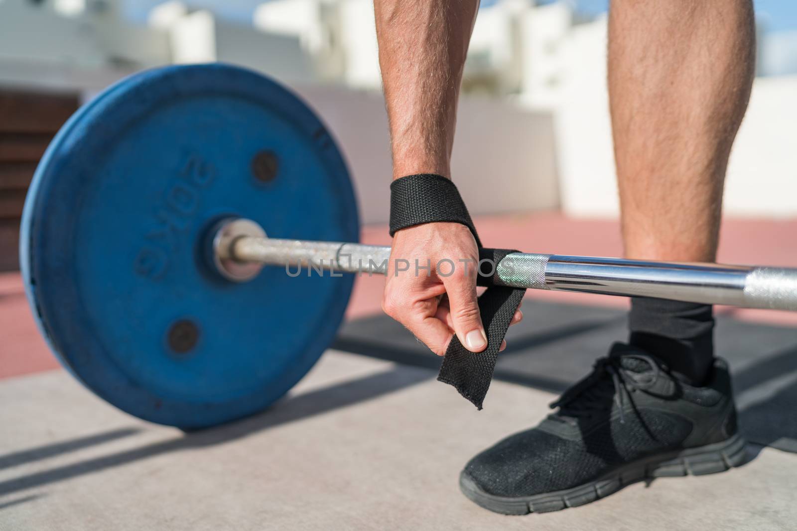 Weightlifting wrist straps support for bodybuilding and powerlifting. Fitness man wearing accessory during barbell weight lifting deadlift exercise workout at gym. Closeup of hand and bar.