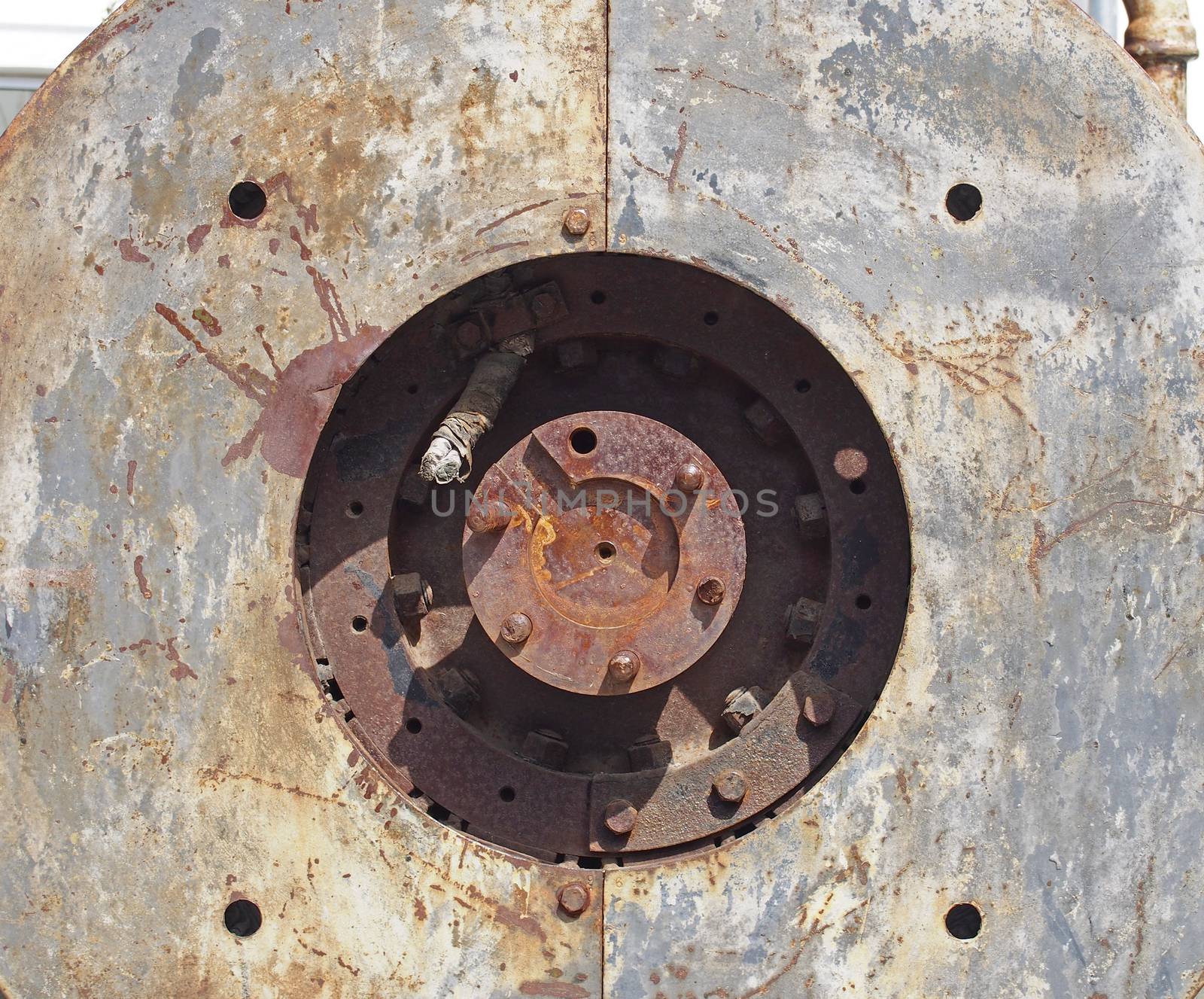 close up full frame detail of old rusting machinery with circular hole in steel plates with bolts and round drive shaft in the center in sunlight and shadow