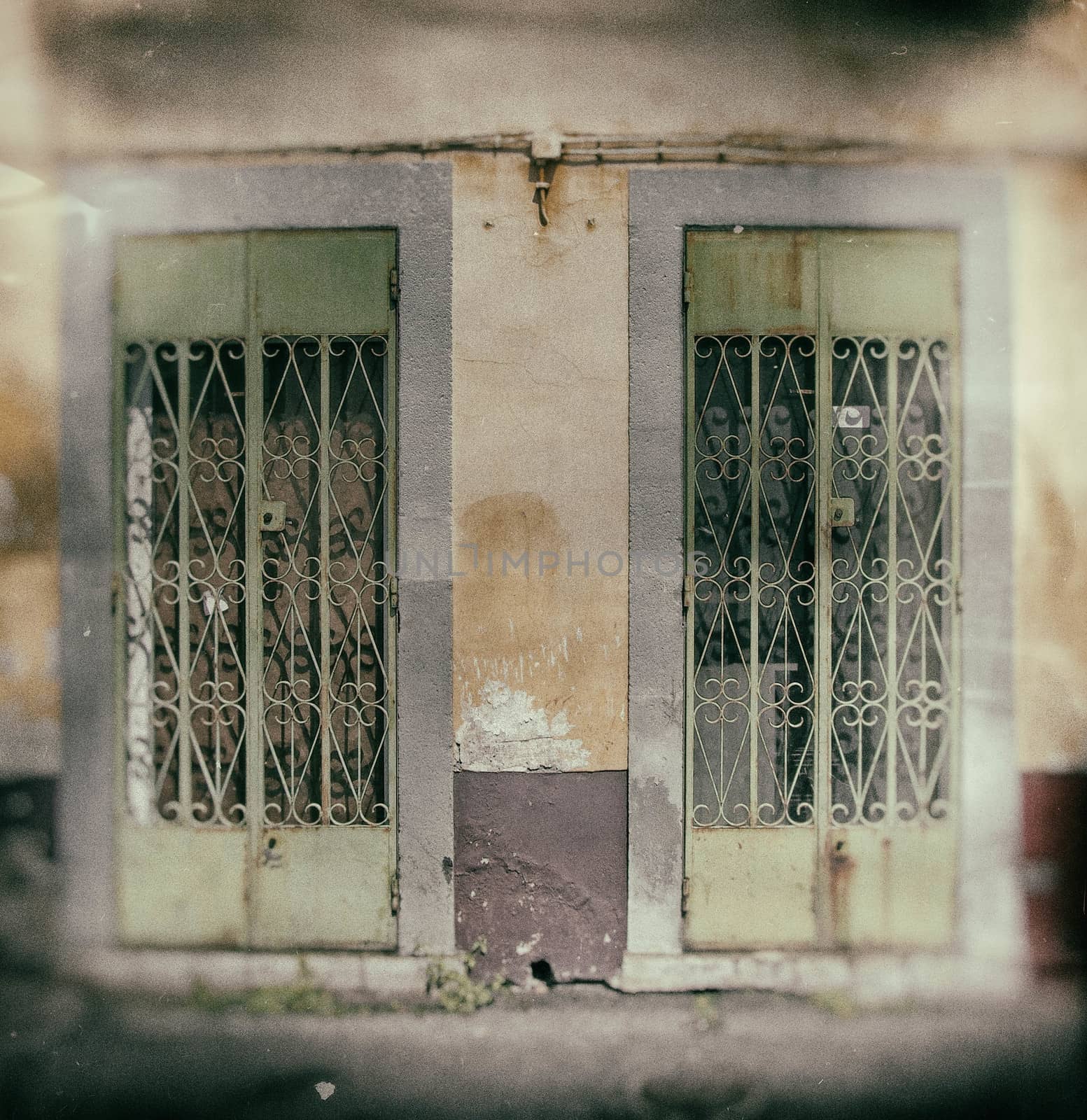 rusting green metal doors with ornate lattice work on the front of a derelict abandoned shop with faded yellow and red walls and shutters in funchal madeira