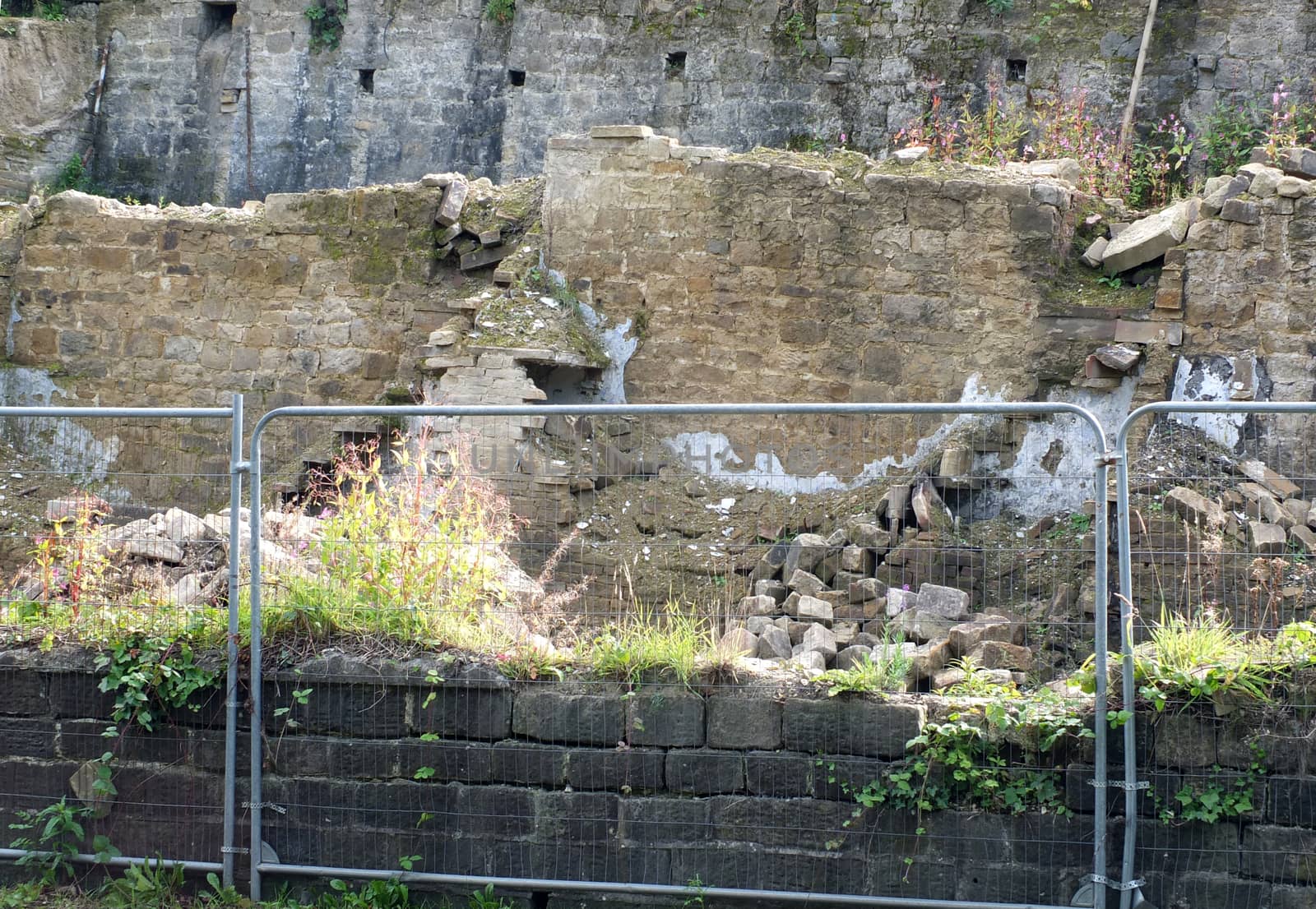 close up of demolished houses on a street with collapsed walls behind a safety fence