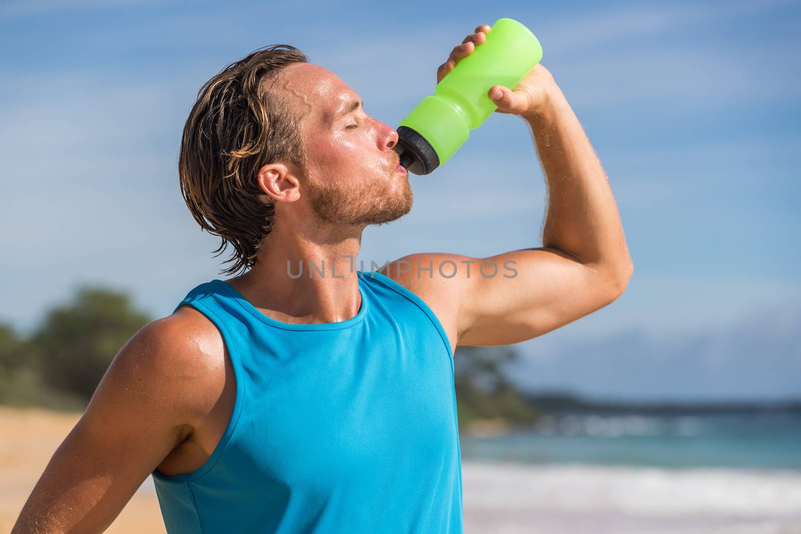 Sports bottle drink sport man drinking water on beach run. Male runner sweaty and thirsty after difficult workout by Maridav