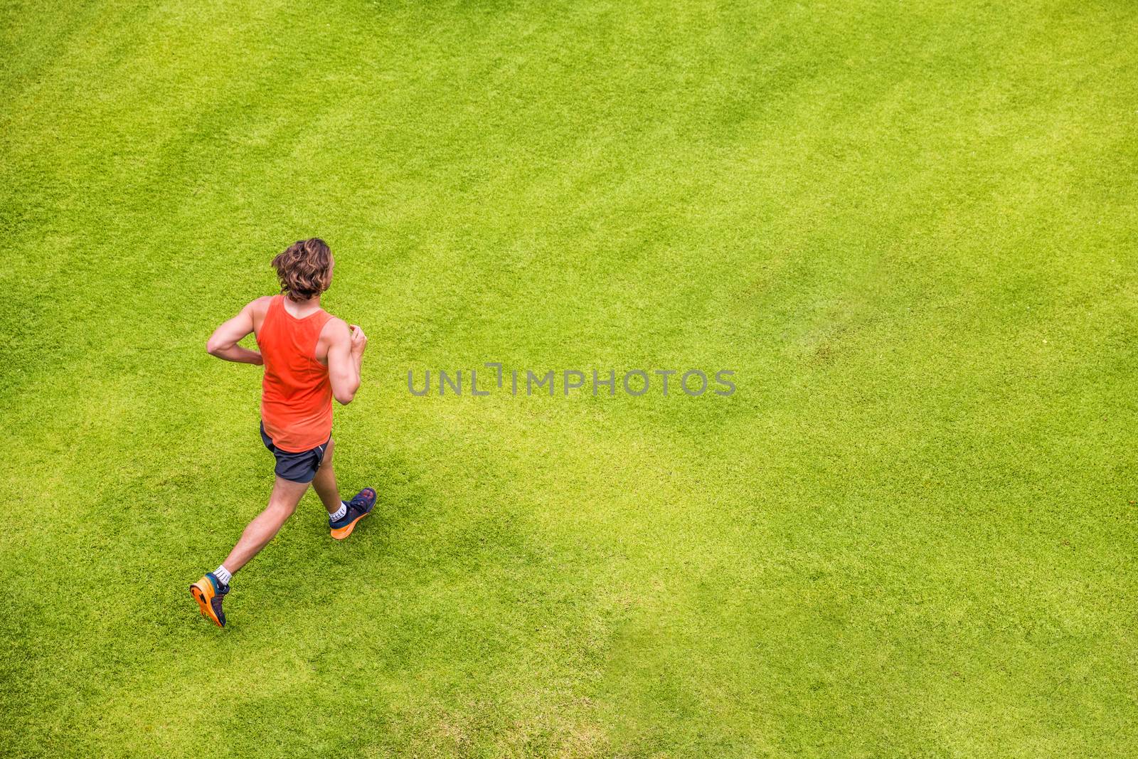 Runner man running on summer grass park jogging healthy lifestyle. People working out cardio top view. Copy space on green texture background.