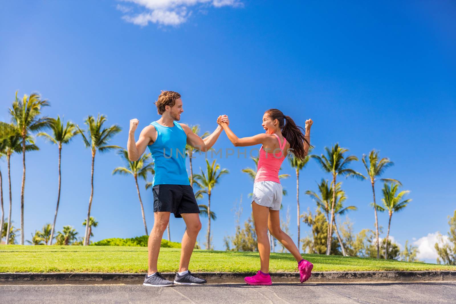 Challenge success runners people high fiving for fitness goal achievement. Athletes couple cheering clapping hands for winning a race. Outdoors sports lifestyle. Personal trainer encouraging girl by Maridav