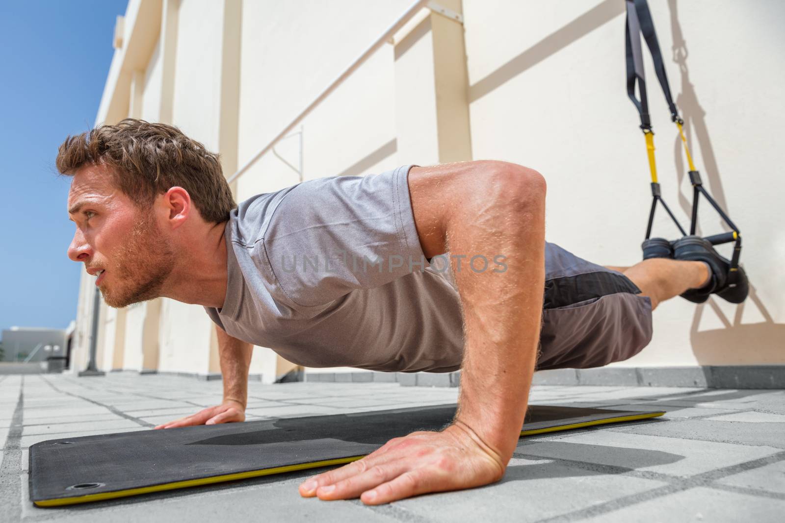 Fitness man doing pushups using suspension straps at fitness centre. Athlete doing bodyweight push-up exercises on floor outdoors by Maridav