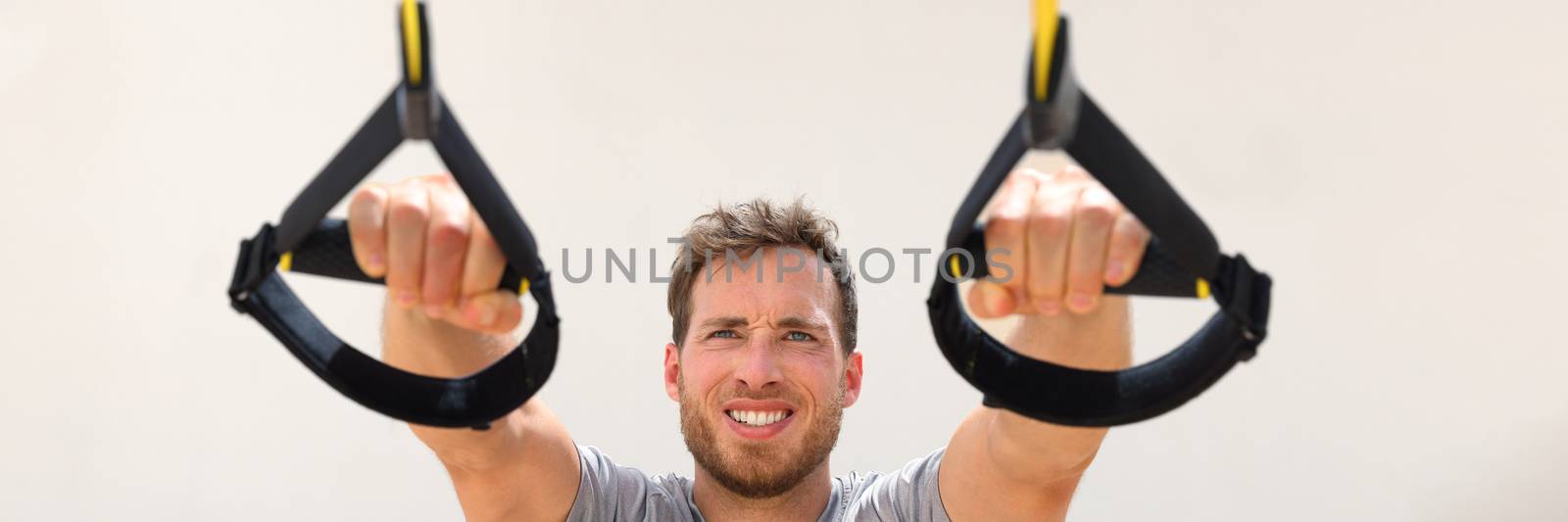 Fitness man trx banner suspension resistance straps training. Athlete holding handles doing inclined pull-ups for back and biceps muscles at gym. Panorama horizontal crop by Maridav