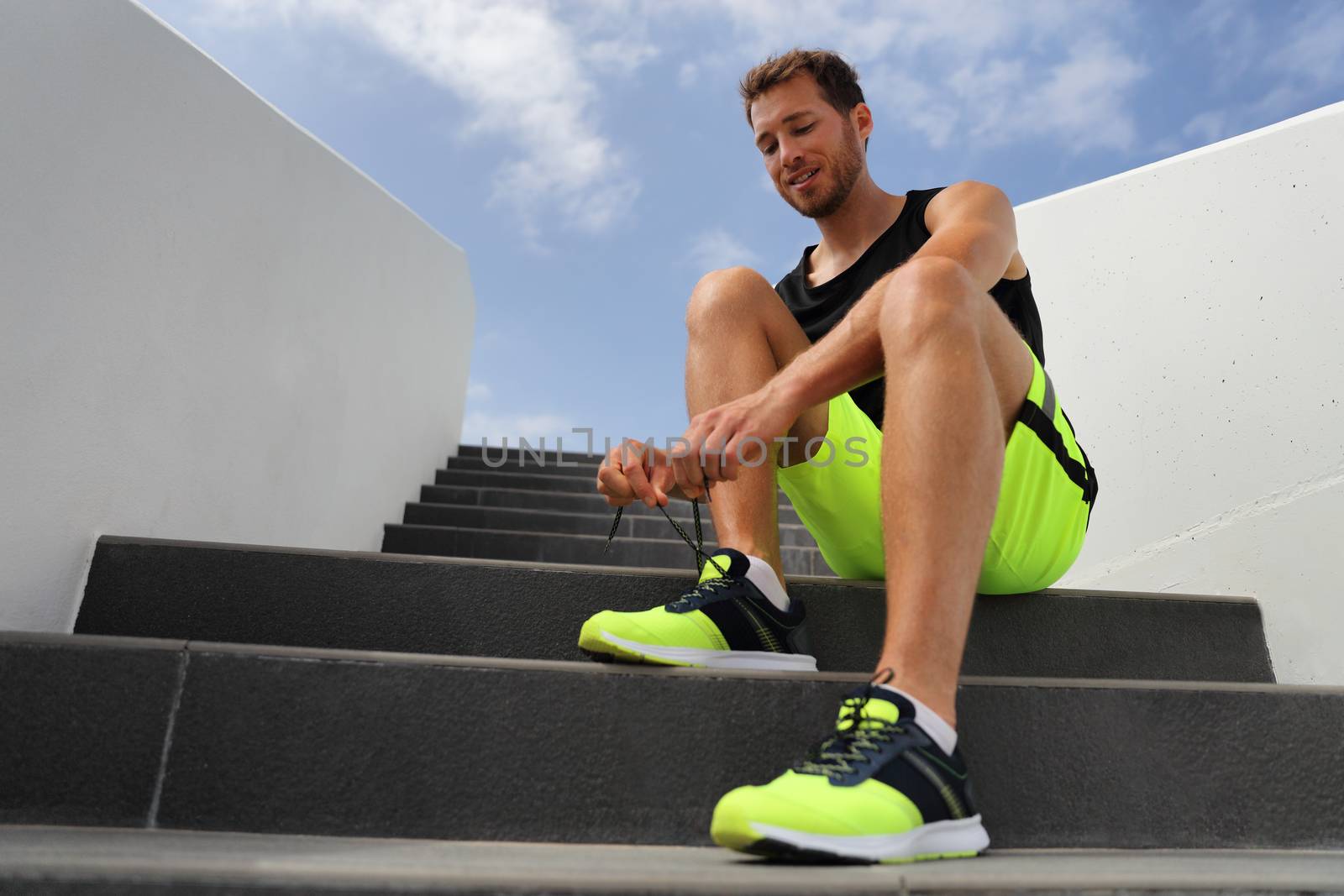 Runner tying running shoes laces getting ready to run on city stairs. Healthy active lifestyle man happy jogging motivation.