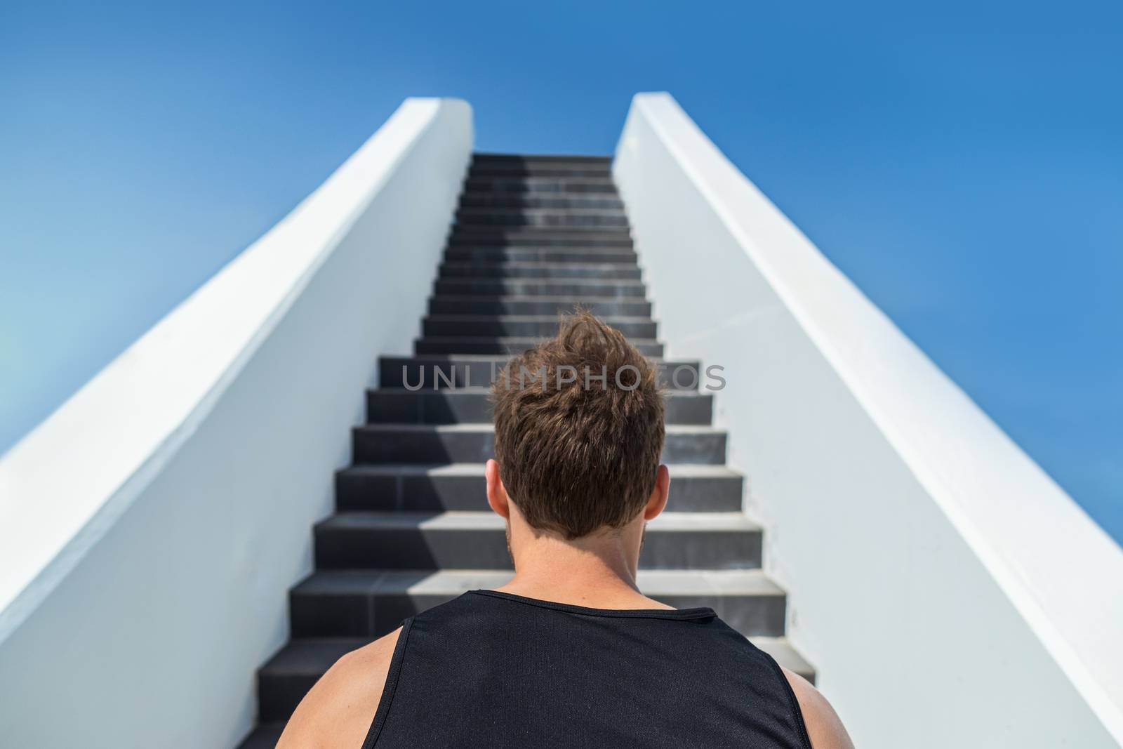 Fitness man looking ahead at stairs climbing challenge. Runner going up running staircase for cardio goal doing weight loss choice in healthy lifestyle. Man choosing difficult path.