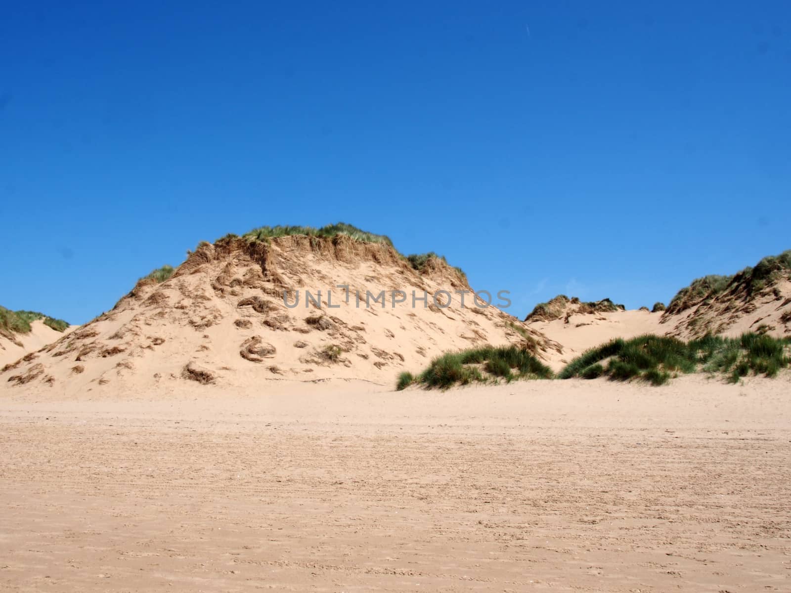 the beach at formby merseyside with tall sand dunes covered in rough grass and a blue summer sunlit sky