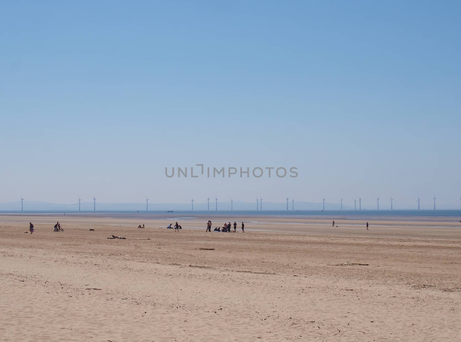 a view of a large flat sand covered summer beach in formby merseyside with unrecognizable people in the middle distance and windmills on the horizon
