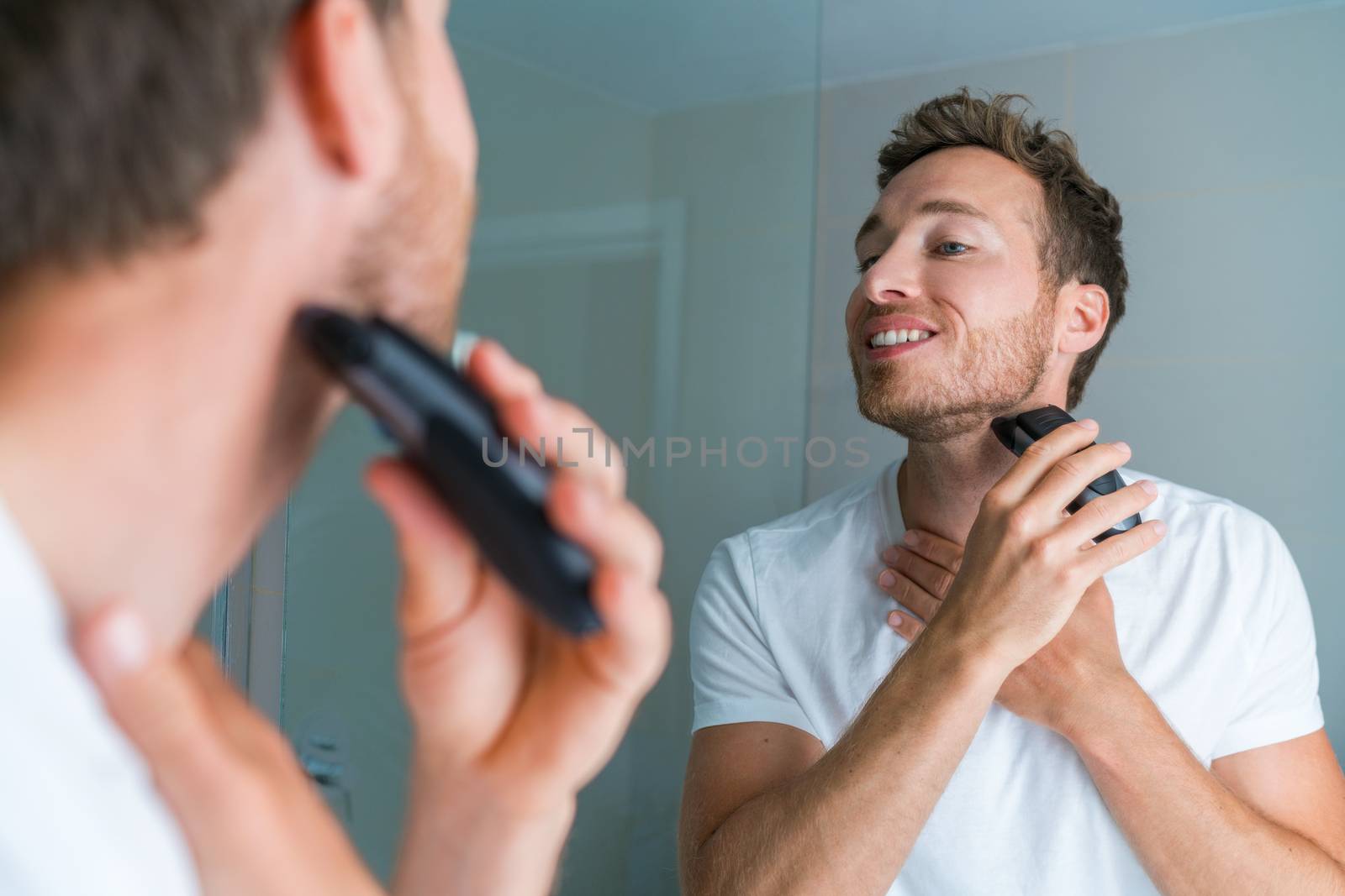 Young man shaving neck and jawline in the morning using electric shaver / clipper. Morning routine modern lifestyle. Male beauty 30s model by Maridav
