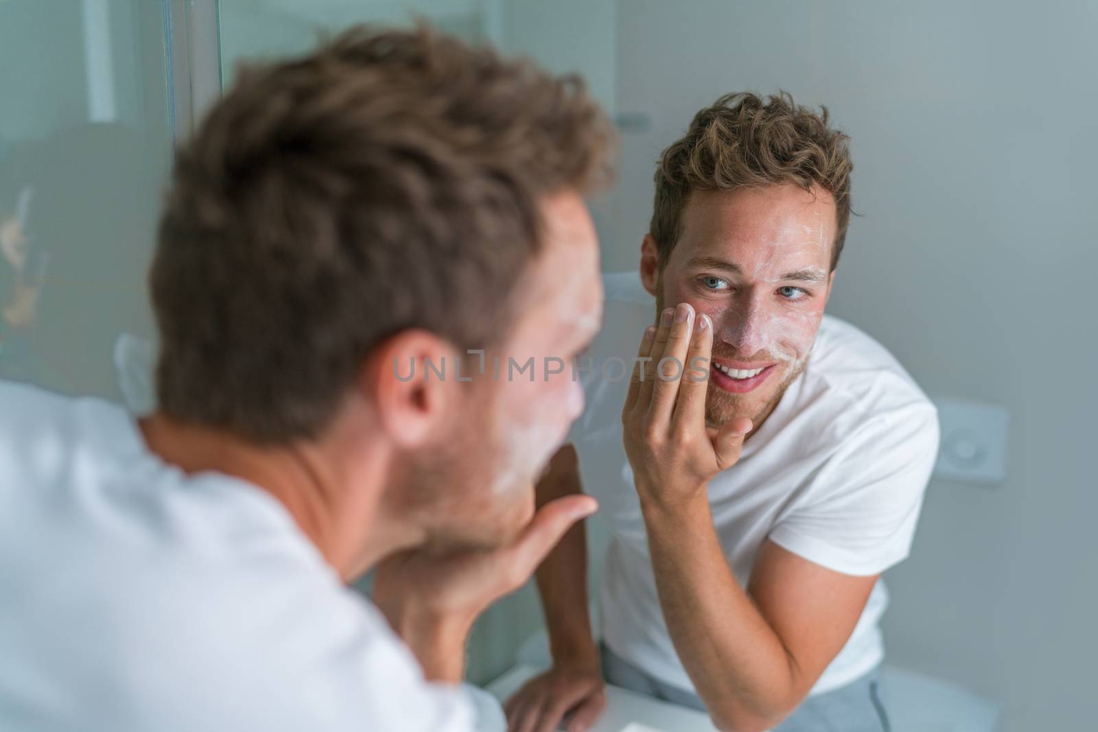 Man washing face with soap scrubbing exfoliation mask facial treatment looking in the mirror. Men taking care of skin, morning face wash routine for cleaning acne pimples by Maridav