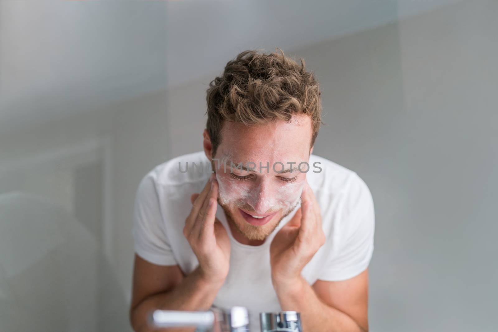 Man washing face with facial cleanser face wash soap in bathroom sink at home.