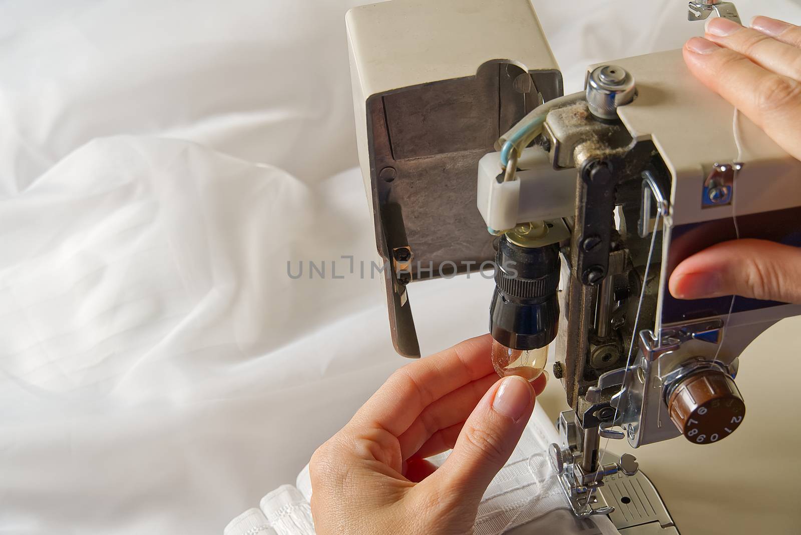 Woman's hands setting sewing machine. worker changing bulb in sewing machine