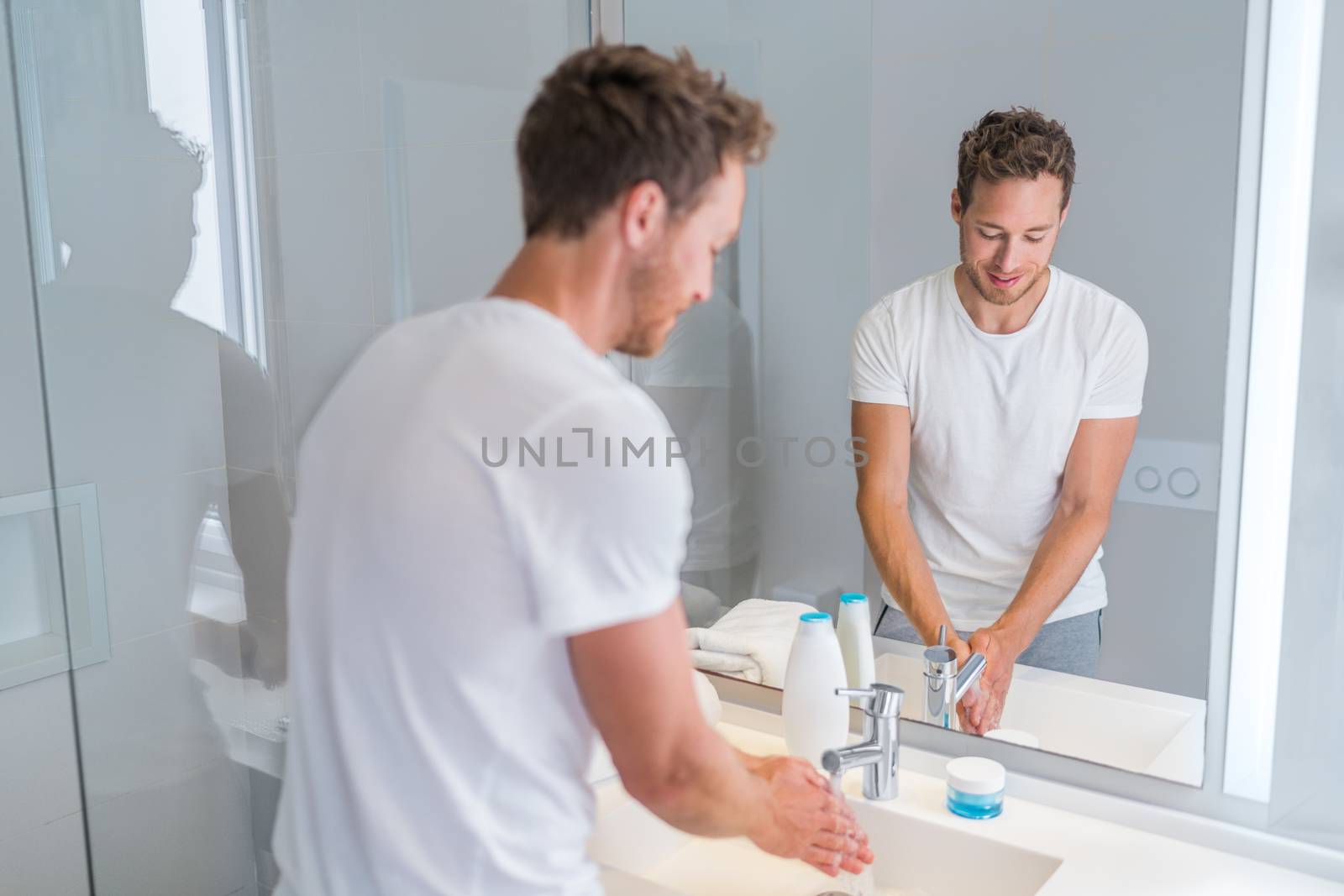 Young man washing hands at home cleaning hand under running water in bathroom sink. House, aparment condo luxury living lifestyle.