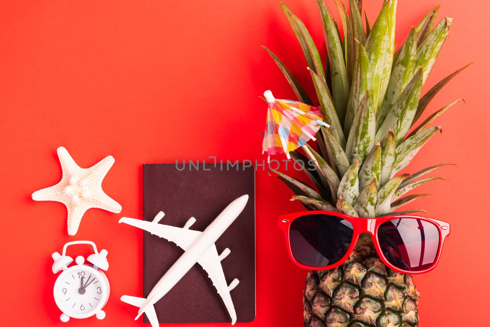 Summer Pineapple Day Concept, Top view flat lay of funny pineapple wear red sunglasses, model plane, starfish, passport and clock alarm isolated on red background, Holiday summertime in tropical
