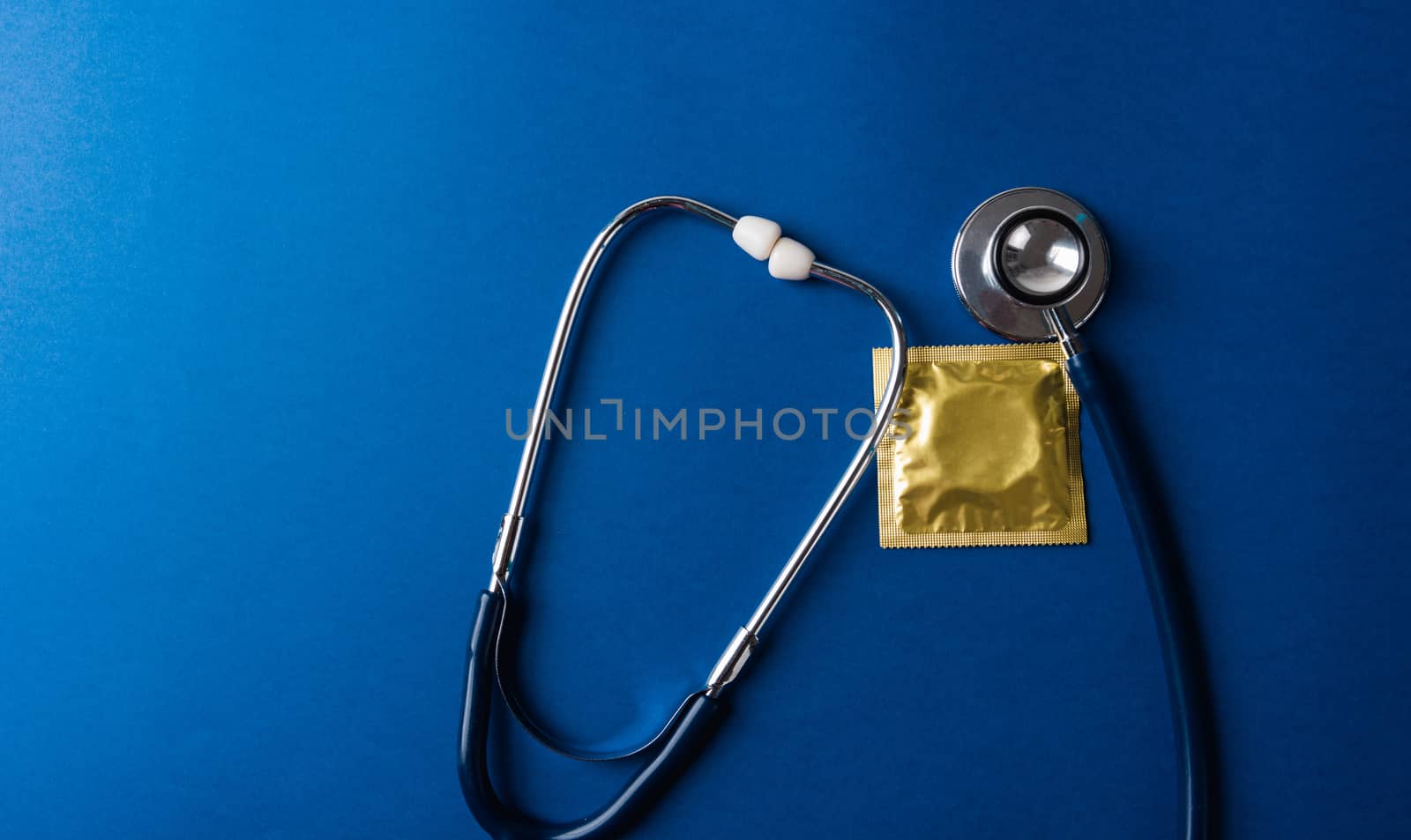 World sexual health or Aids day, Top view flat lay medical equipment, condom in pack and stethoscope, studio shot isolated on dark blue background, Safe sex and reproductive health concept