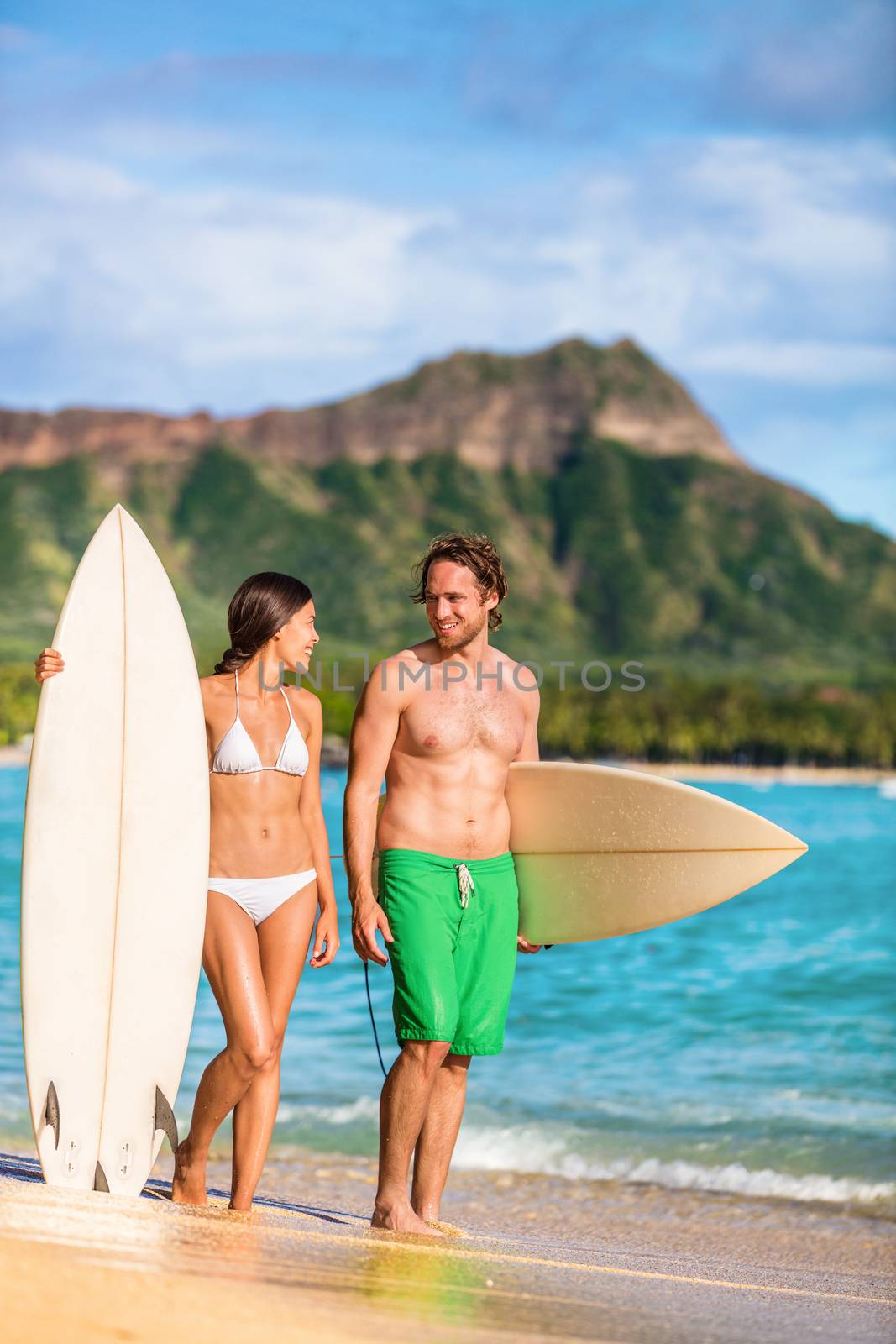 Beach couple surfing in Hawaii relaxing at sunset standing with surfboards on waikiki beach, Honolulu, Oahu, USA. Summer holidays travel landscape. Happy people having fun.
