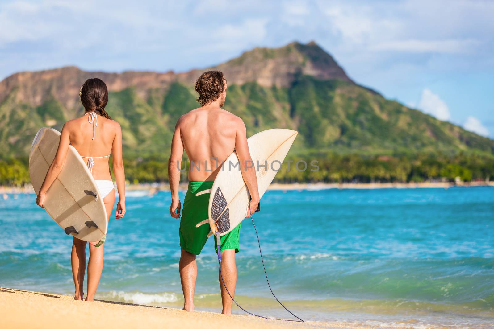 Hawaii surfers people relaxing on waikiki beach with surfboards looking at waves in Honolulu, Hawaii. Healthy active lifestyle fitness couple at sunset with diamond head mountain in the background by Maridav