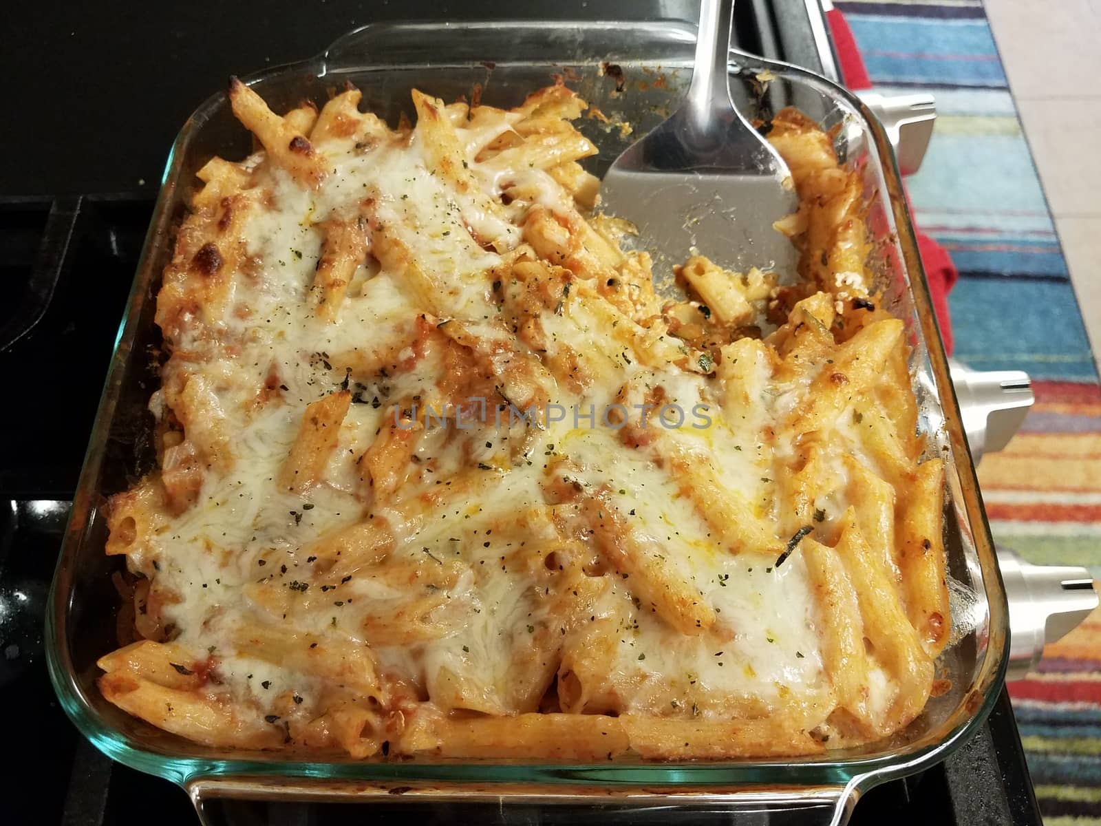 Italian penne pasta with cheese in glass container with spatula on stove