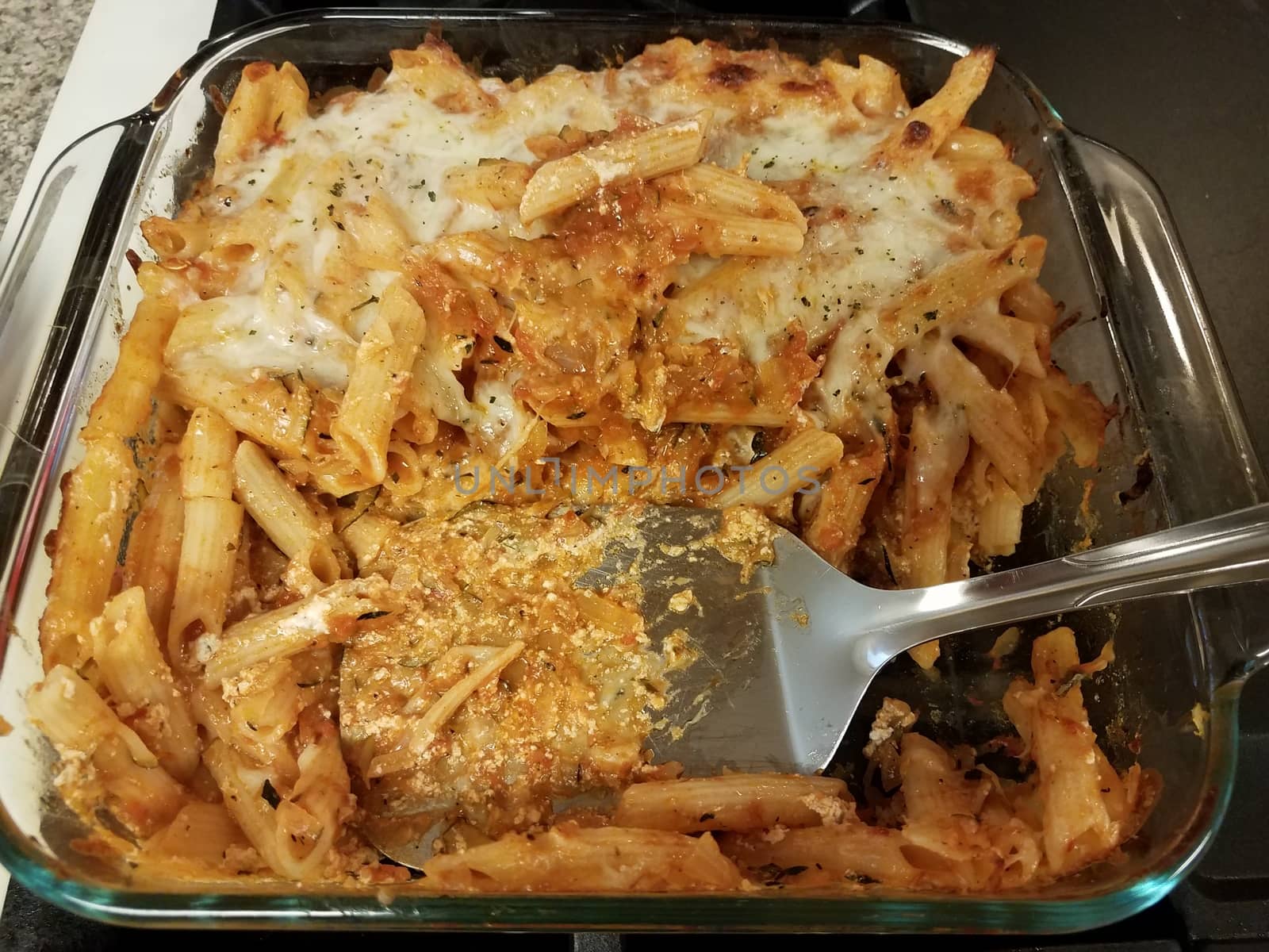 Italian penne pasta with cheese in glass container with spatula on stove