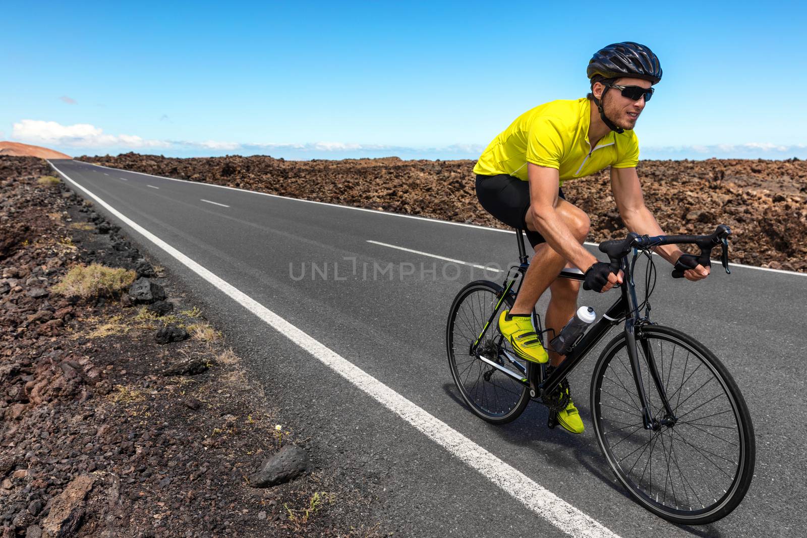 Road bike cyclist man biking riding racing bicycle training for triathlon race. Sports athlete biking on road working out cardio living active and healthy lifestyle.