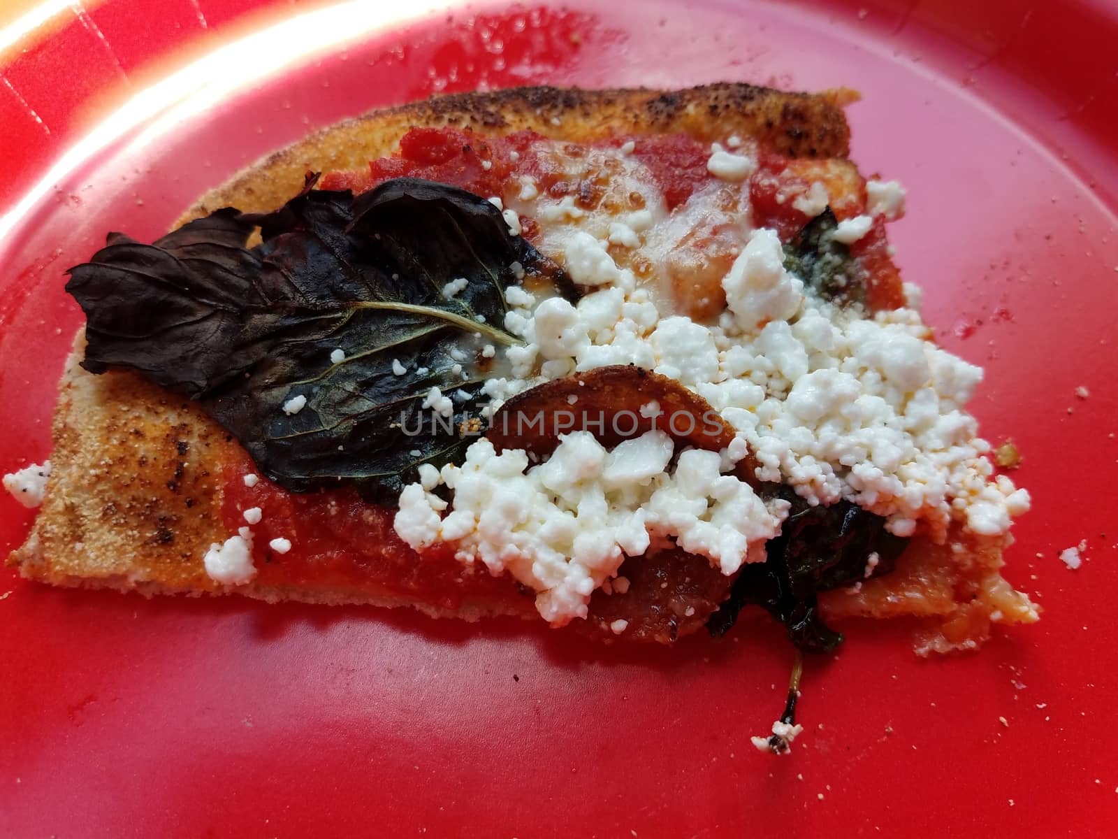 basil leaf and goat cheese on slice of pizza on red plate