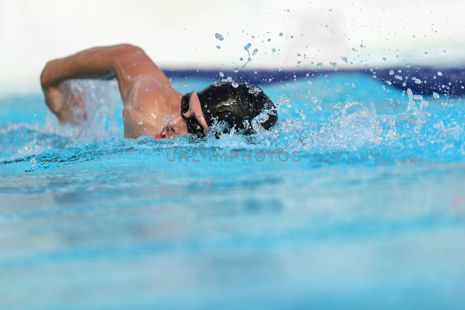 Swimming pool athlete training indoors for professional competition. Swimmer man on swim practice in stadium doing crawl with arm splashing water. Copy space on blue water background by Maridav