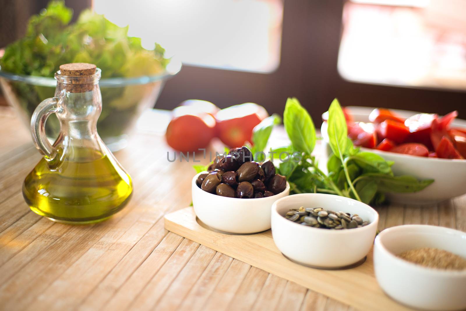 Extra virgin olive oil and olives in the foreground with fresh vegetables and sunlight in the background - Mediterranean diet concept - Healthy summer food concept