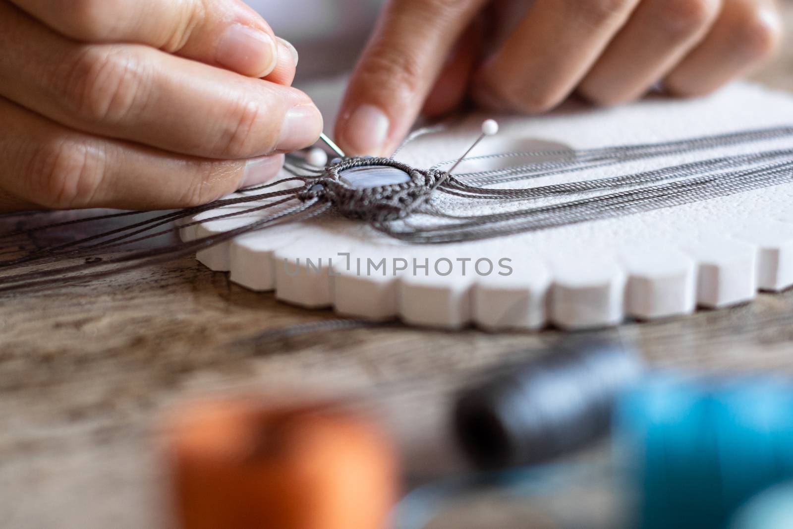 Detailed macro close-up of woman fingers working on a handmade knotted micro macrame bracelet with blurred spools of thread in bokeh effect - Working from home to reinvent your life concept by robbyfontanesi