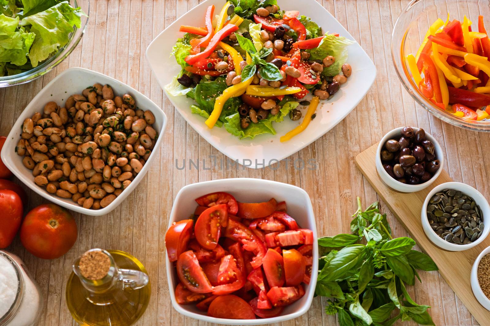 Flat lay top view of a compound fresh salad plate with vegetable ingredients all around it on a light wooden table and natural sunlight - Fresh healthy vegan food concept by robbyfontanesi