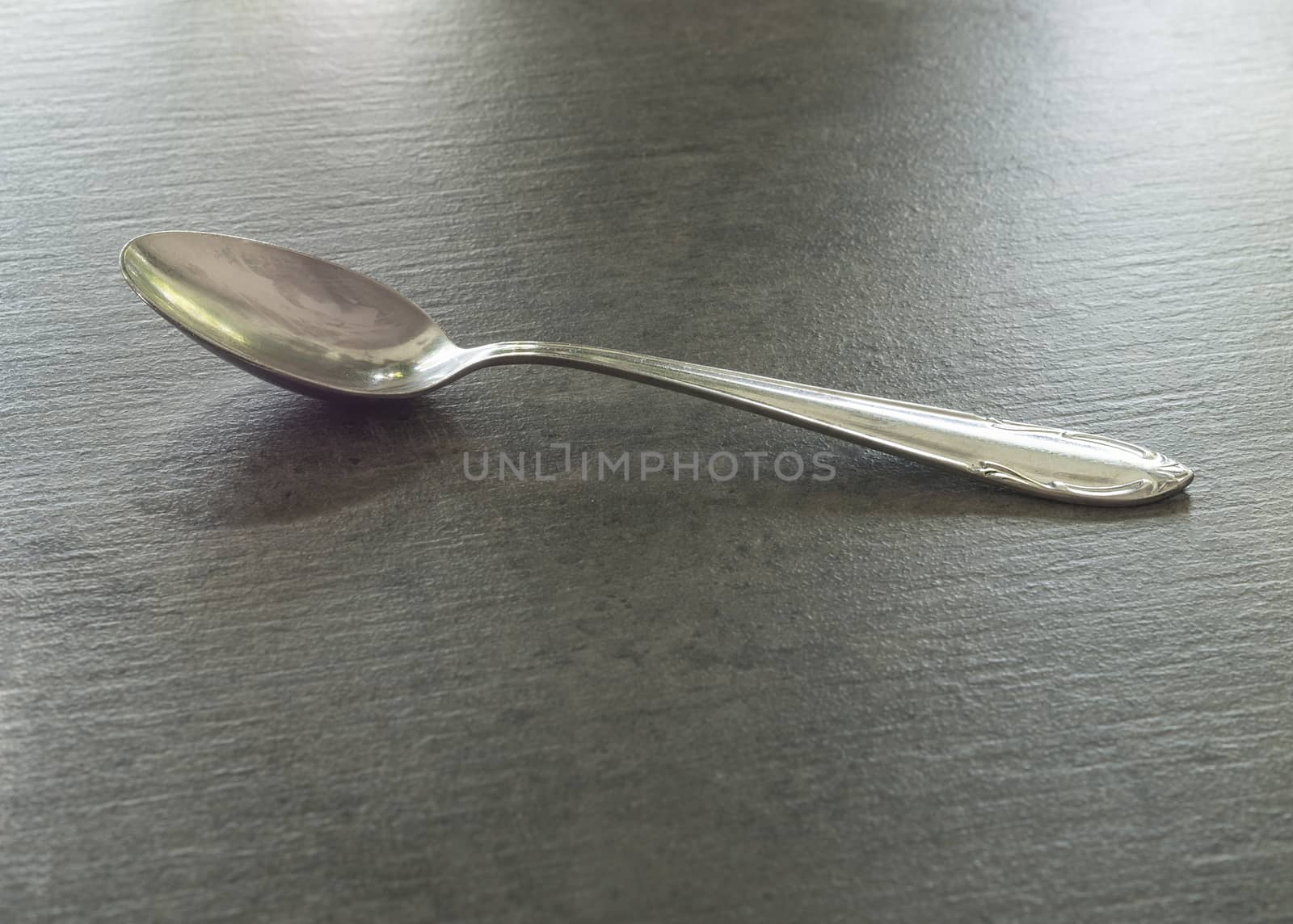 close up one silver steel tea spoon on a grey textured background