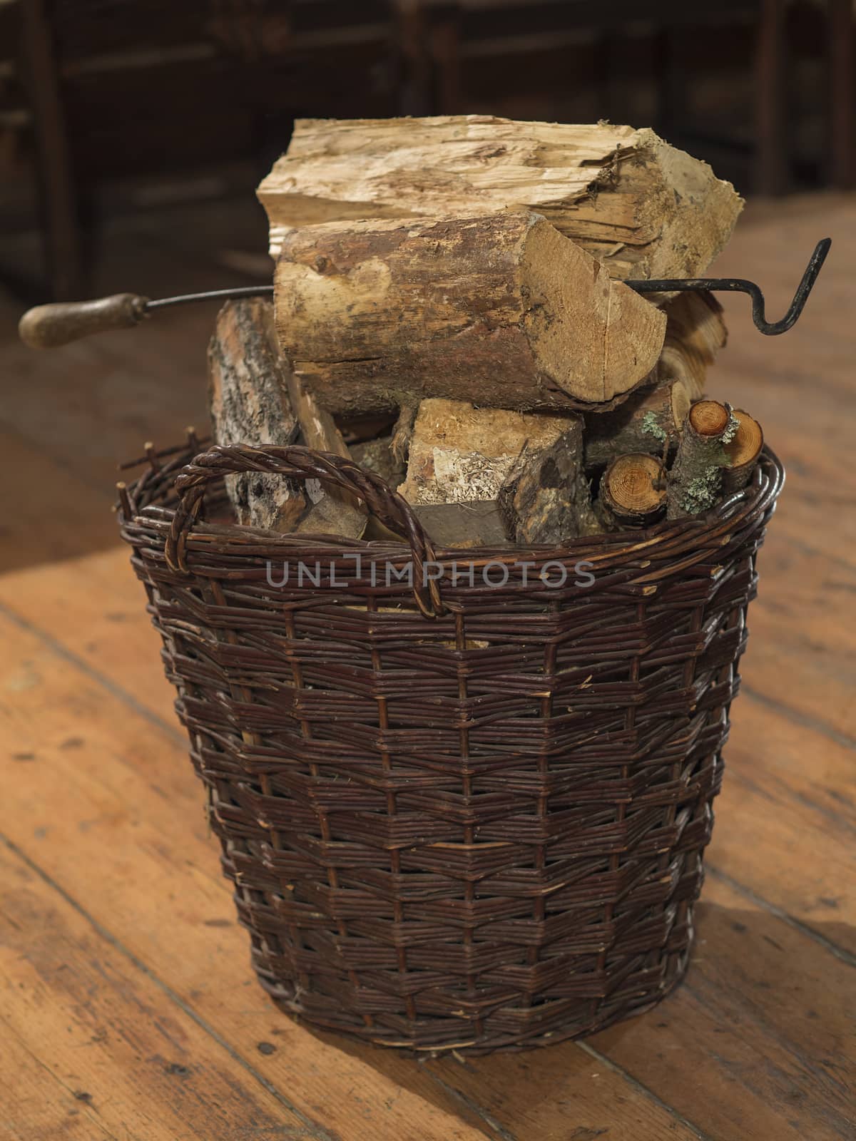 wicker basket full of chopped wood and fire-hook on wooden board floor